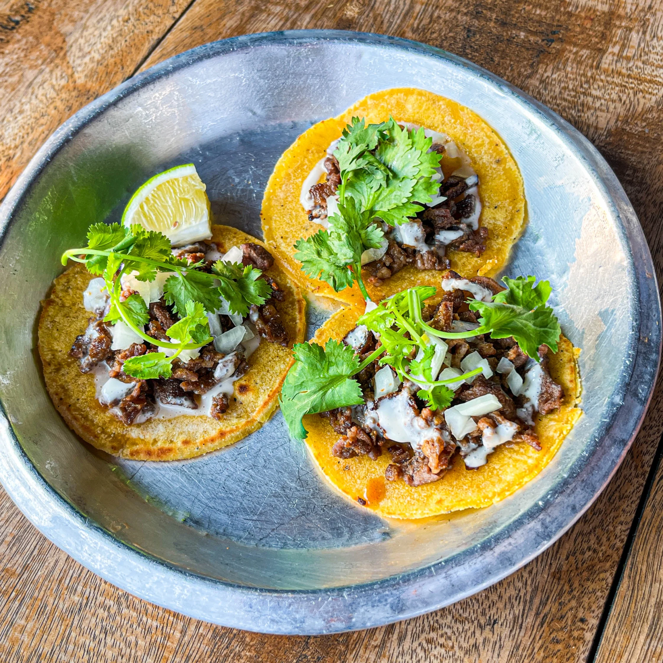 Drive-By Taco Shop’s beef sirloin steak tacos topped with chopped onions, cilantro, and creamy sauce, served with a lime wedge.