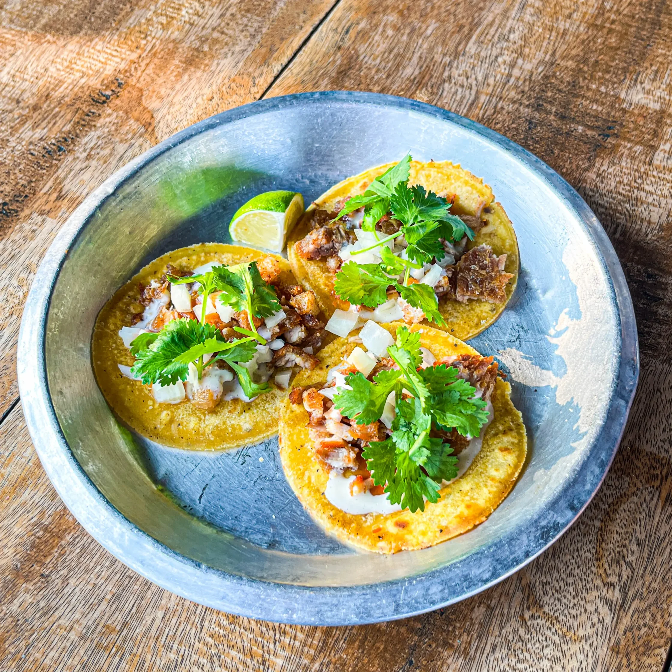 Drive-By Taco Shop’s chicharones tacos topped with chopped pork, onions, cilantro, and sauce, served with a lime wedge.