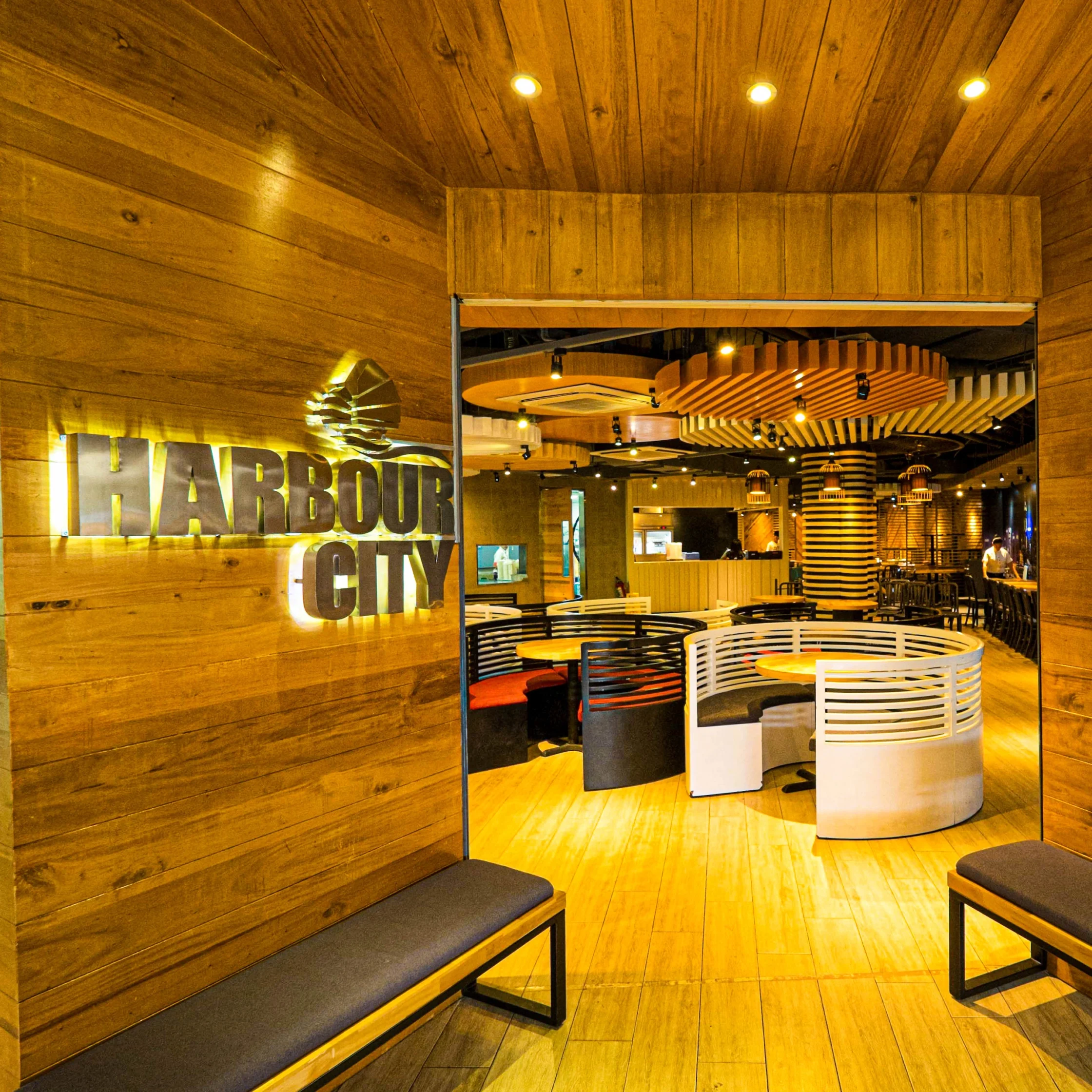 Interior entrance of Harbour City restaurant featuring wooden walls, illuminated signage, and modern seating inside the dining area.