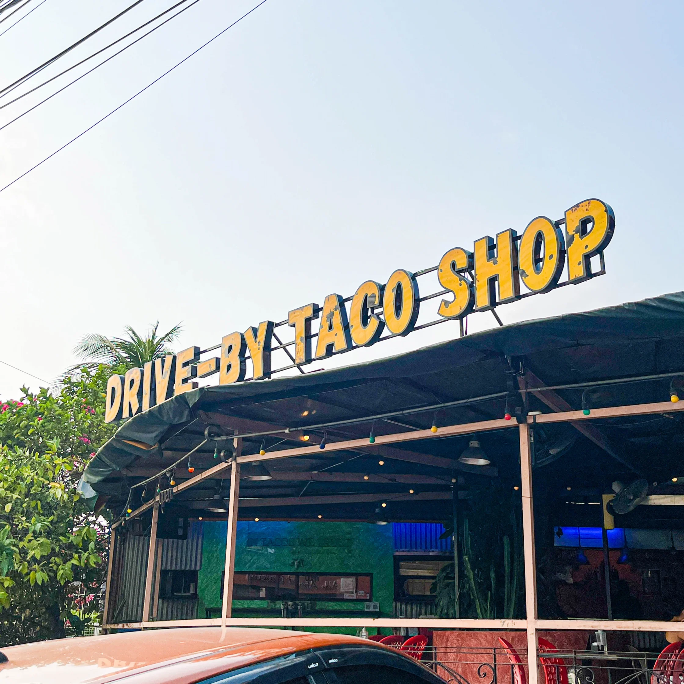 Exterior of Drive-By Taco Shop in BF Homes, Parañaque, featuring the large yellow “DRIVE-BY TACO SHOP” sign above the open-air dining area.