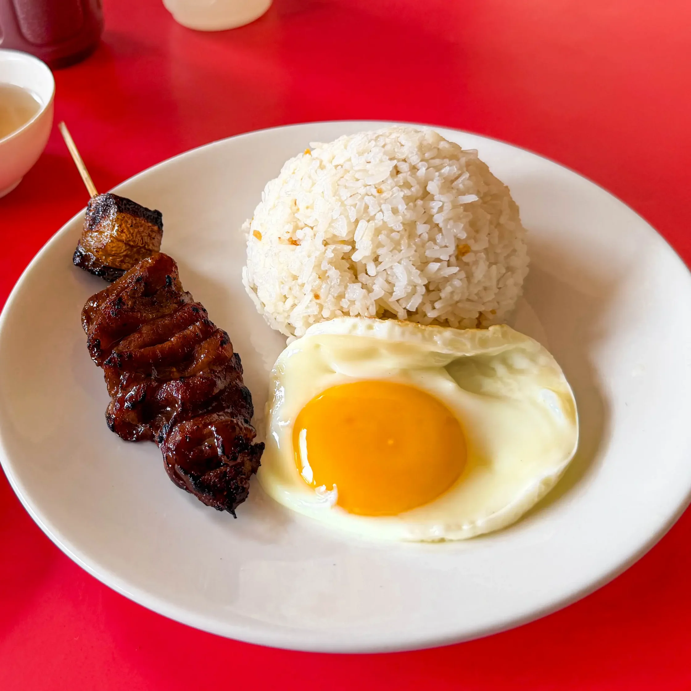 Maty’s barsilog meal featuring grilled pork barbecue on a stick, garlic fried rice, and a sunny-side-up egg served on a white plate.