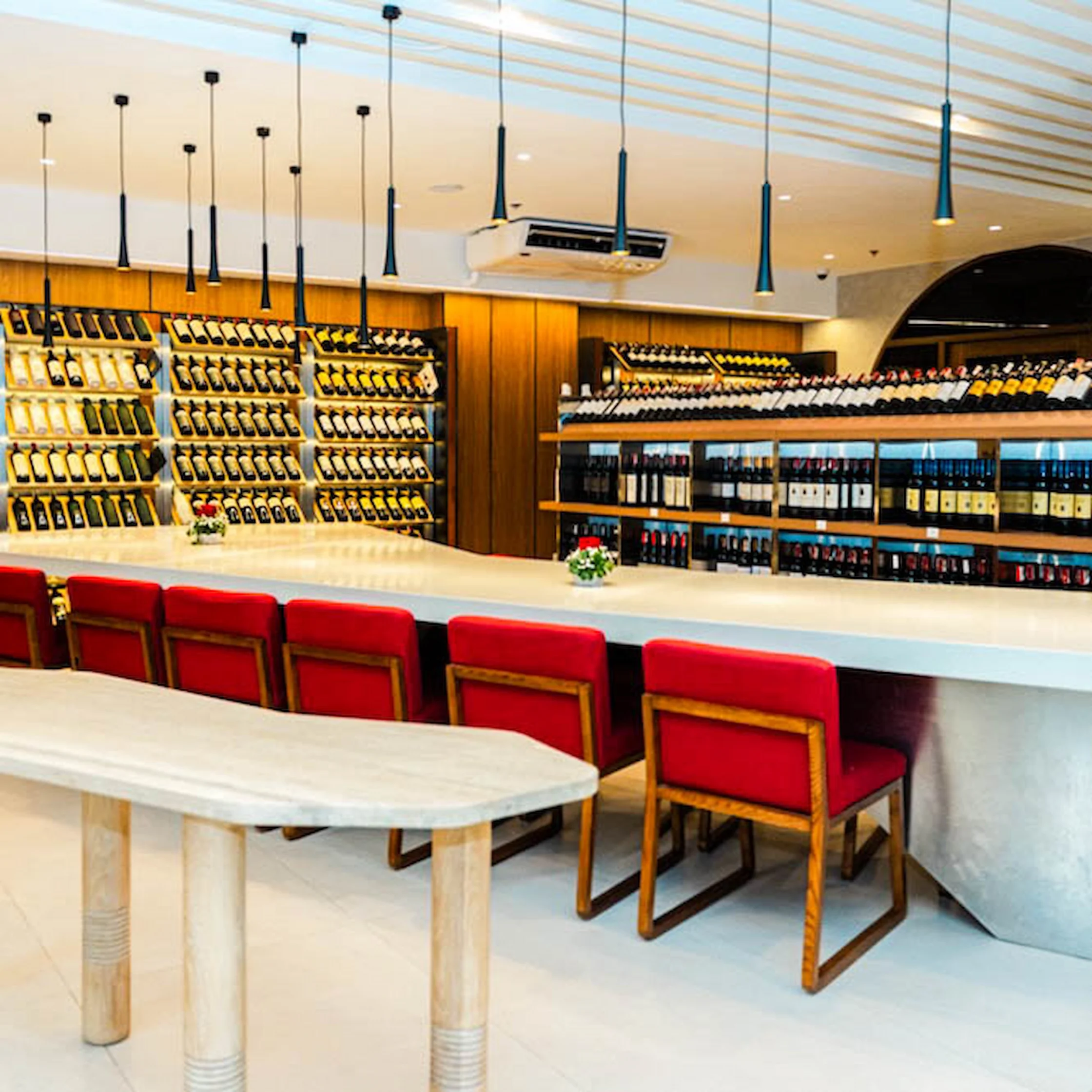 Ground-floor interior of Dominion Cellar Makati featuring a wine shop and bistro area with a long counter, red chairs, and shelves lined with wine bottles.