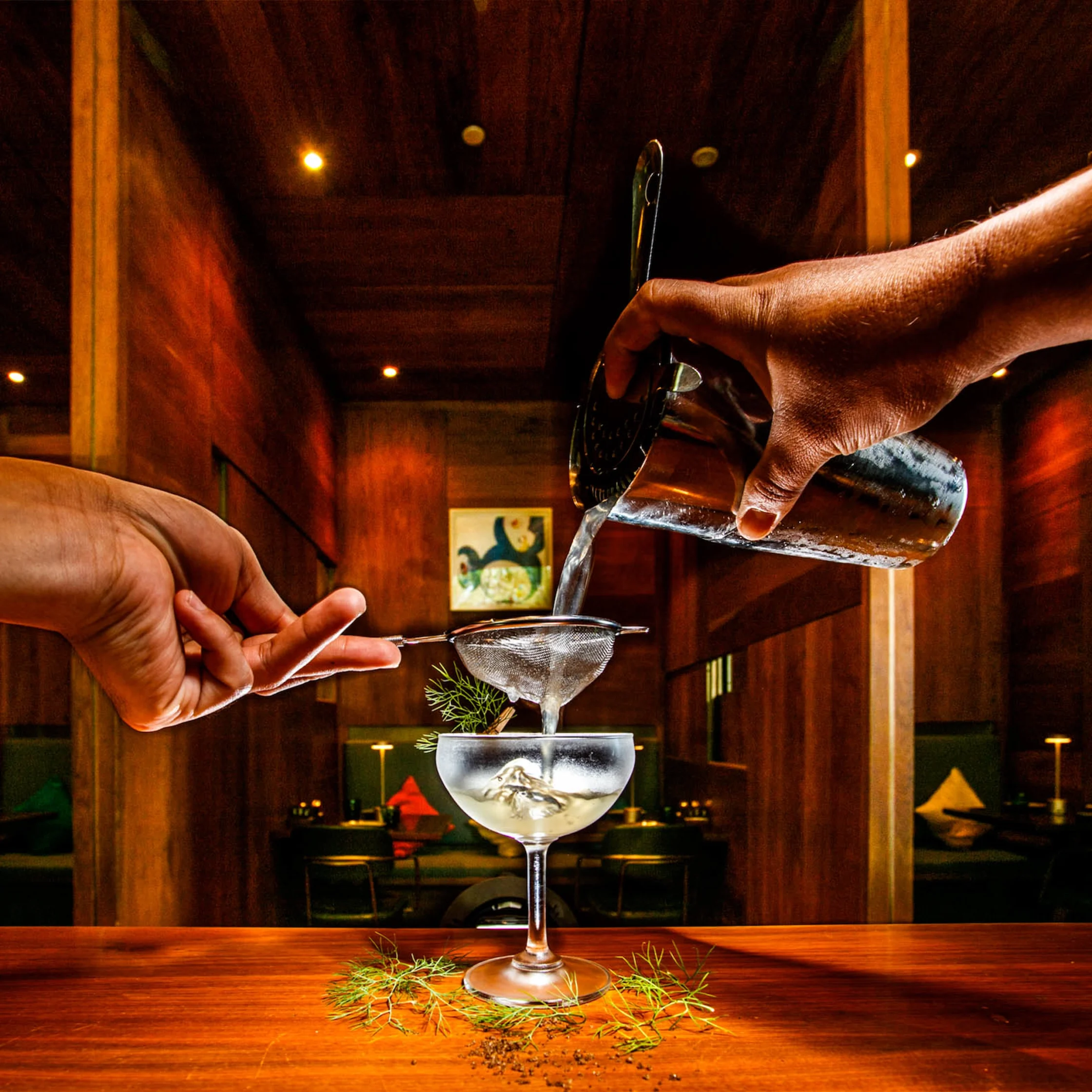 The Pig & Palm Cebu’s Dill or No Dill cocktail being poured through a strainer into a coupe glass at the bar.