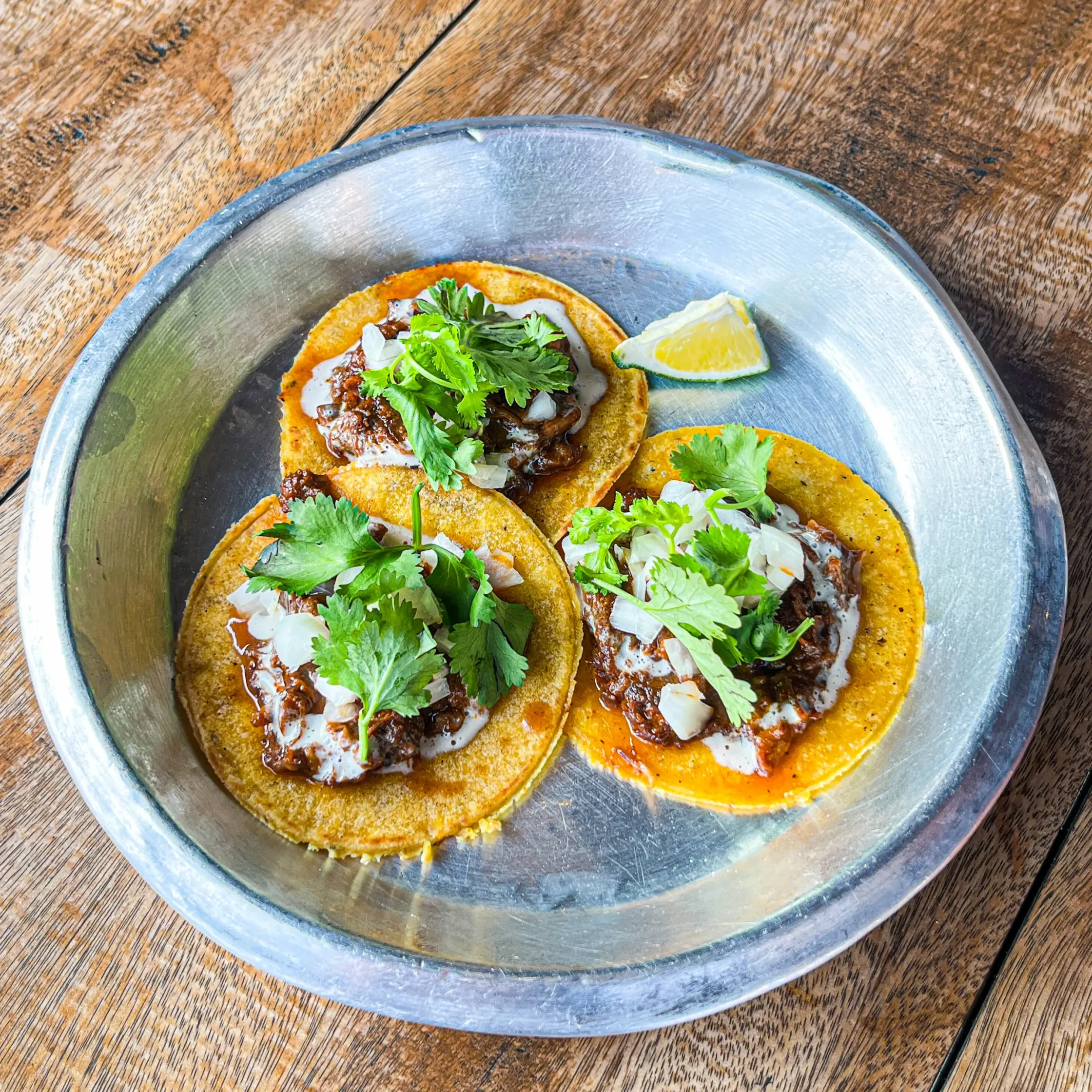 Drive-By Taco Shop’s white adobo-style pulled pork butt tacos topped with onions, cilantro, and creamy sauce, served with a lime wedge.