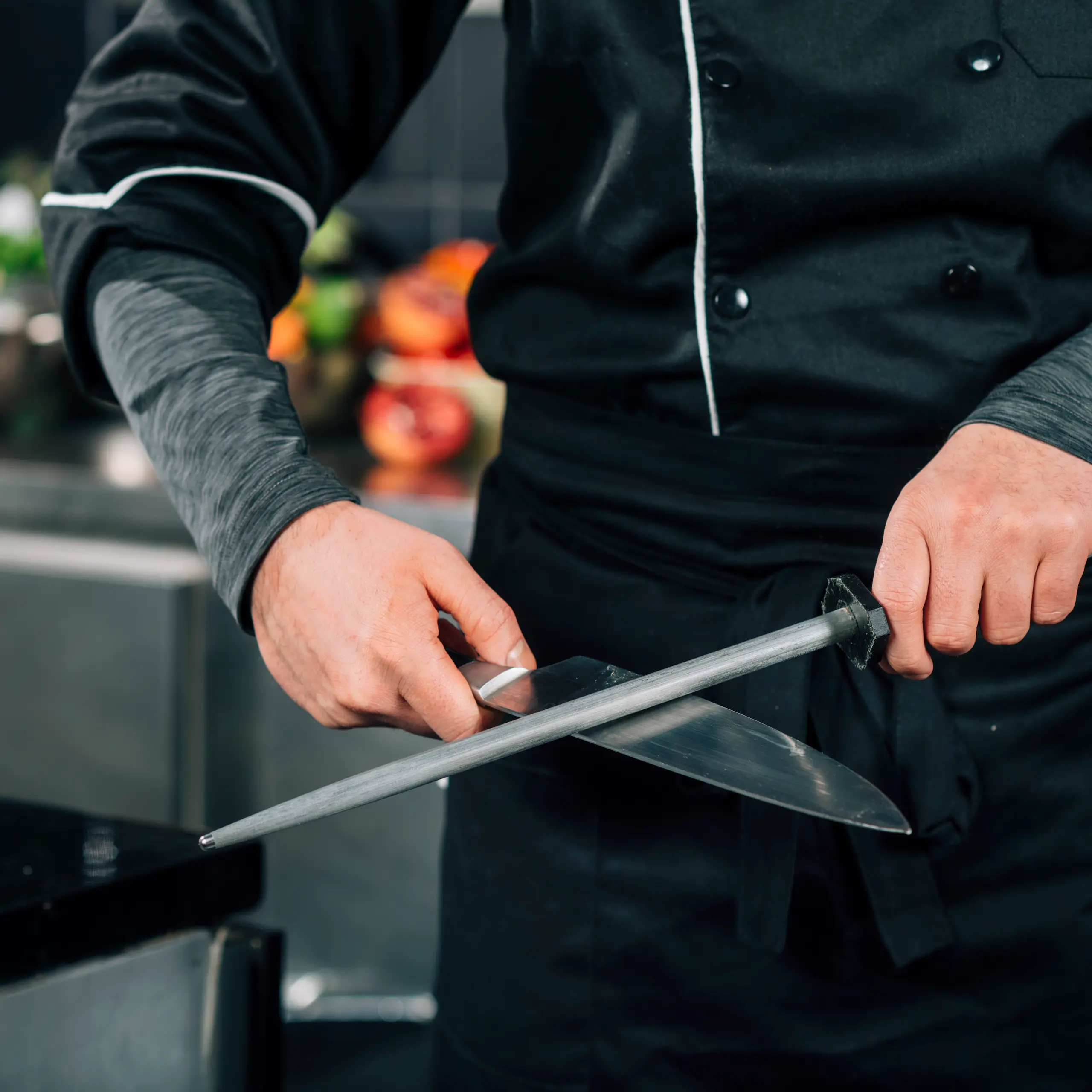 Chef sharpening a kitchen knife using a honing steel in a professional kitchen.