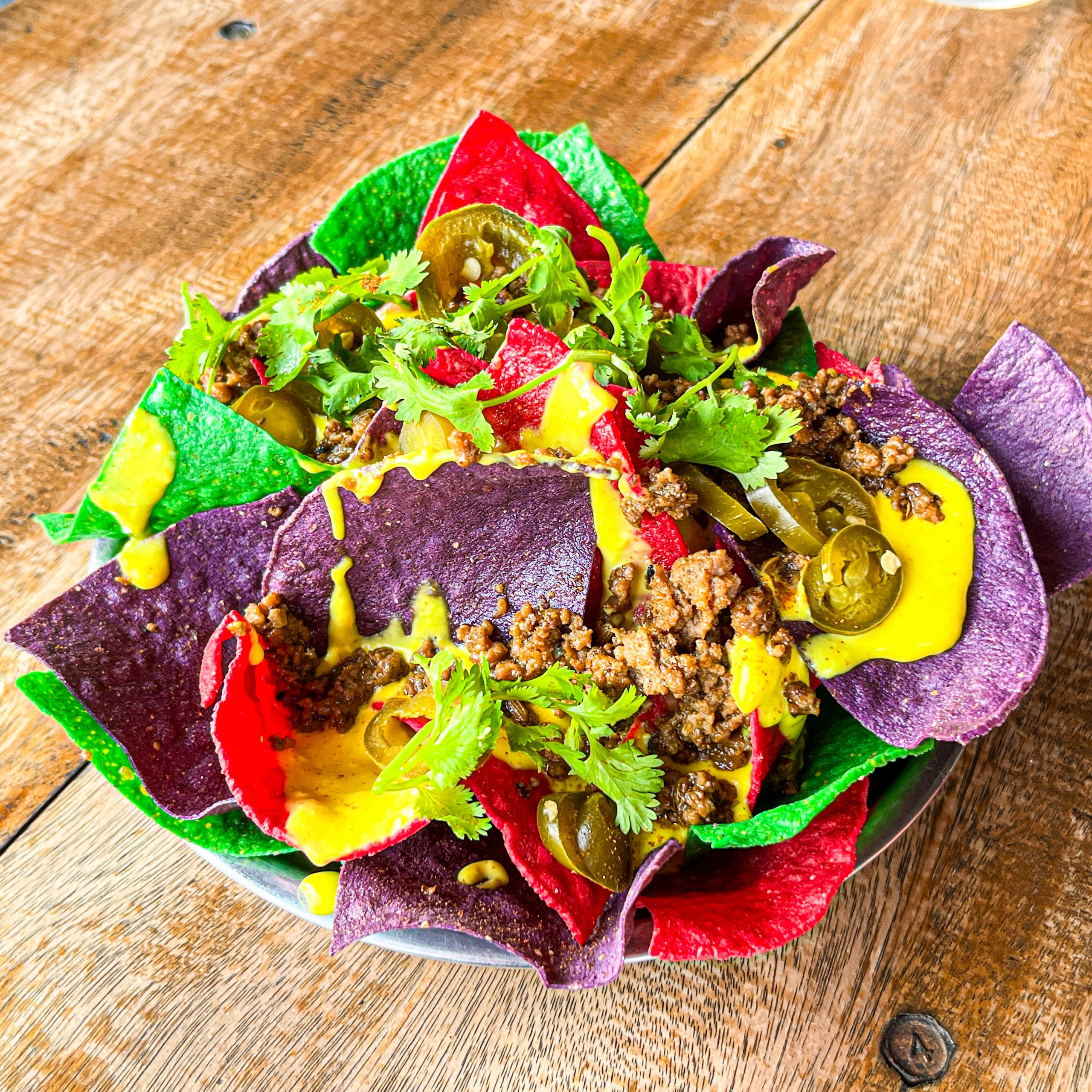 Drive-By Taco Shop’s beef nachos topped with seasoned ground beef, jalapeños, cilantro, and cheese sauce, served with colorful tortilla chips.
