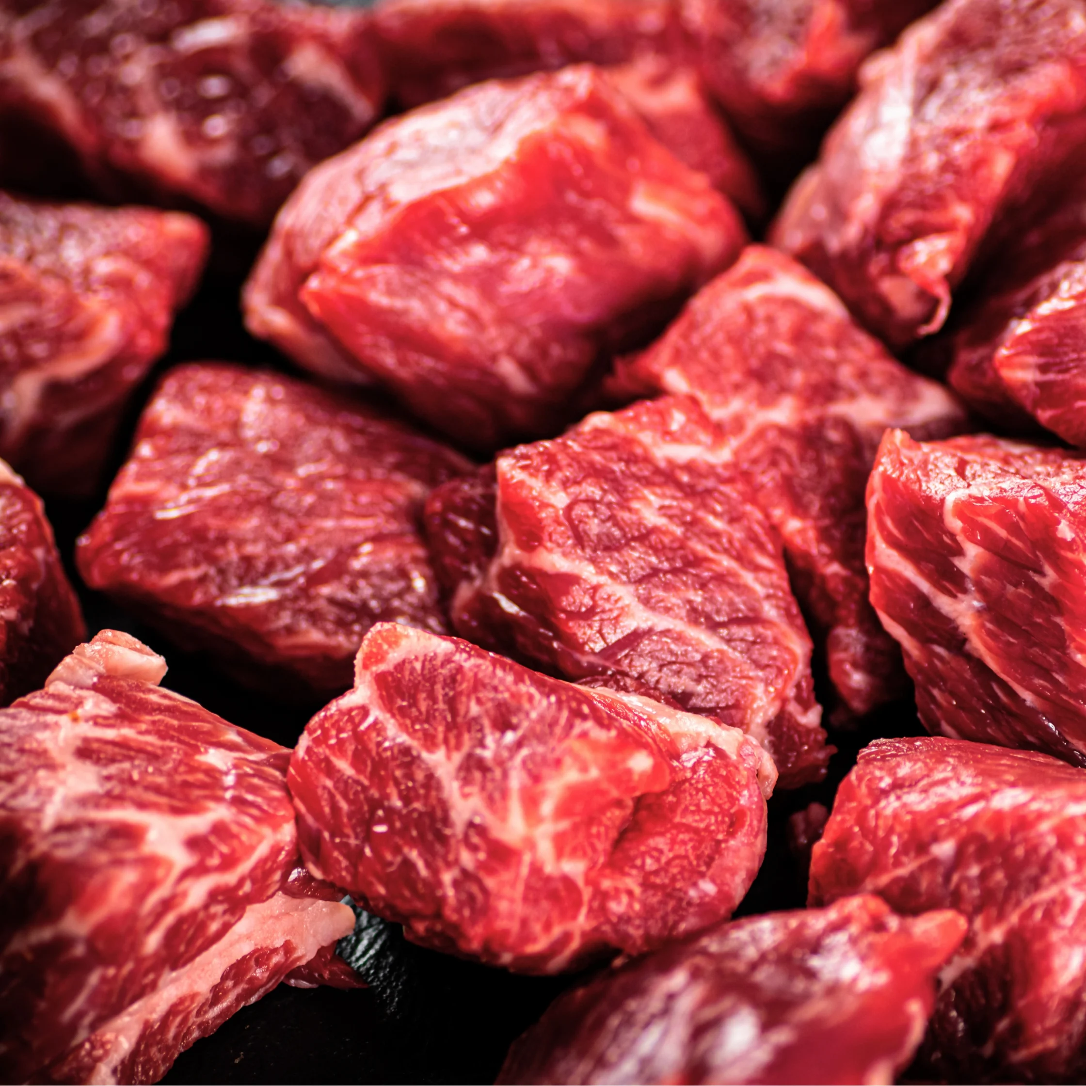 Raw beef cubes with marbling piled on a dark surface, ready for cooking.