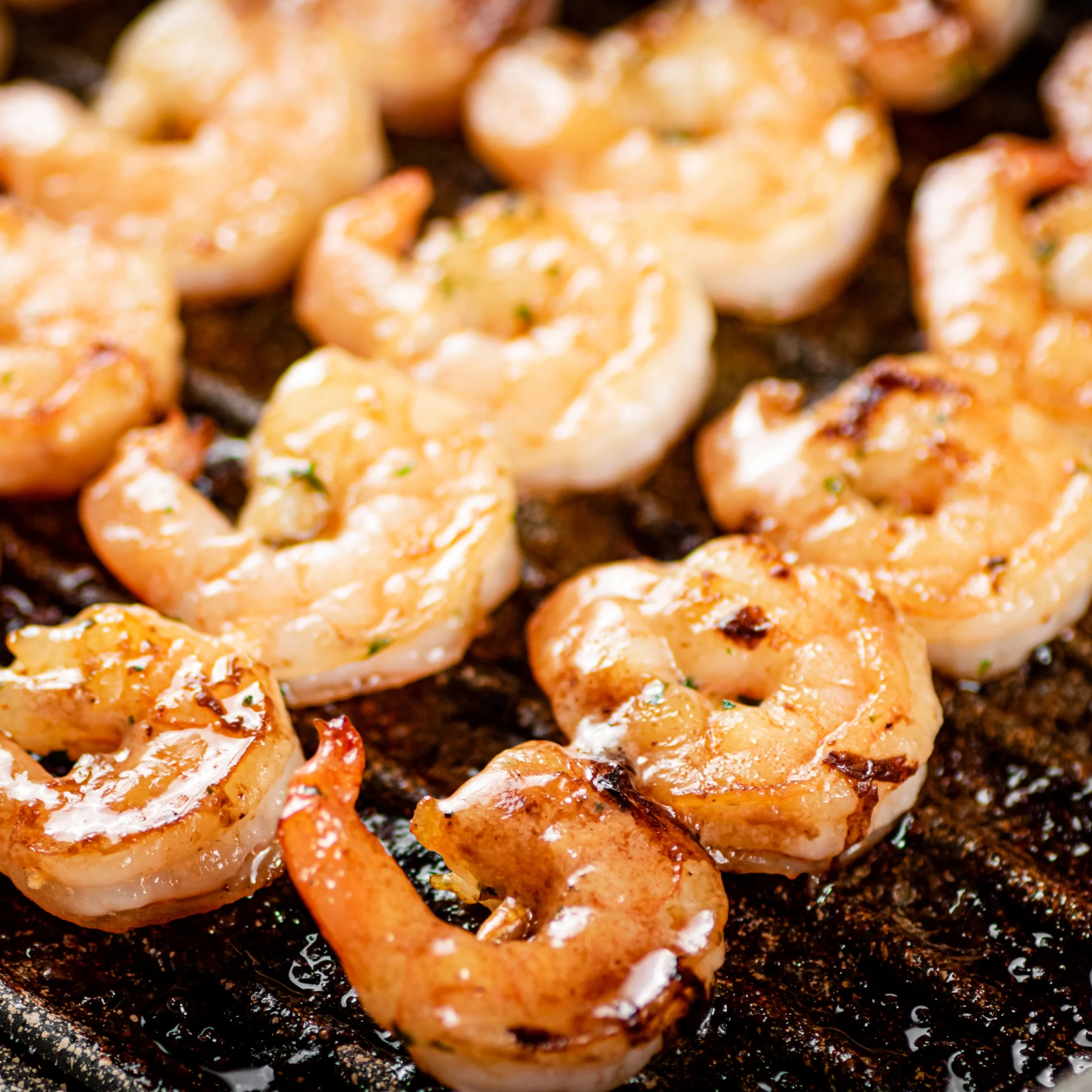 Golden brown shrimp sizzling in a dark skillet, brushed with garlic and herbs.