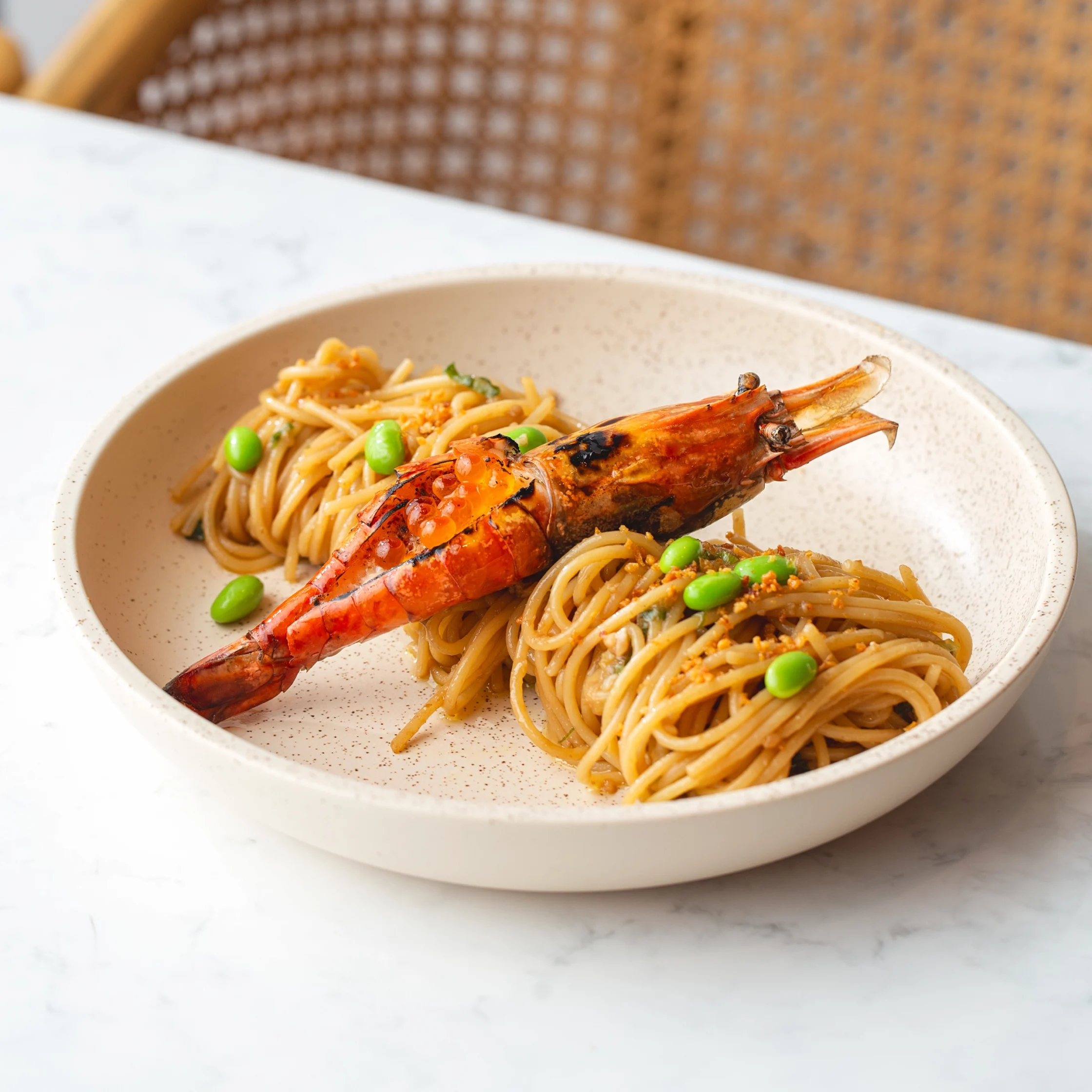 Flour Pot's Shrimp and Ikura Pasta. Linguine pasta with green edamame surrounding a large grilled shrimp laid across a speckled beige plate.