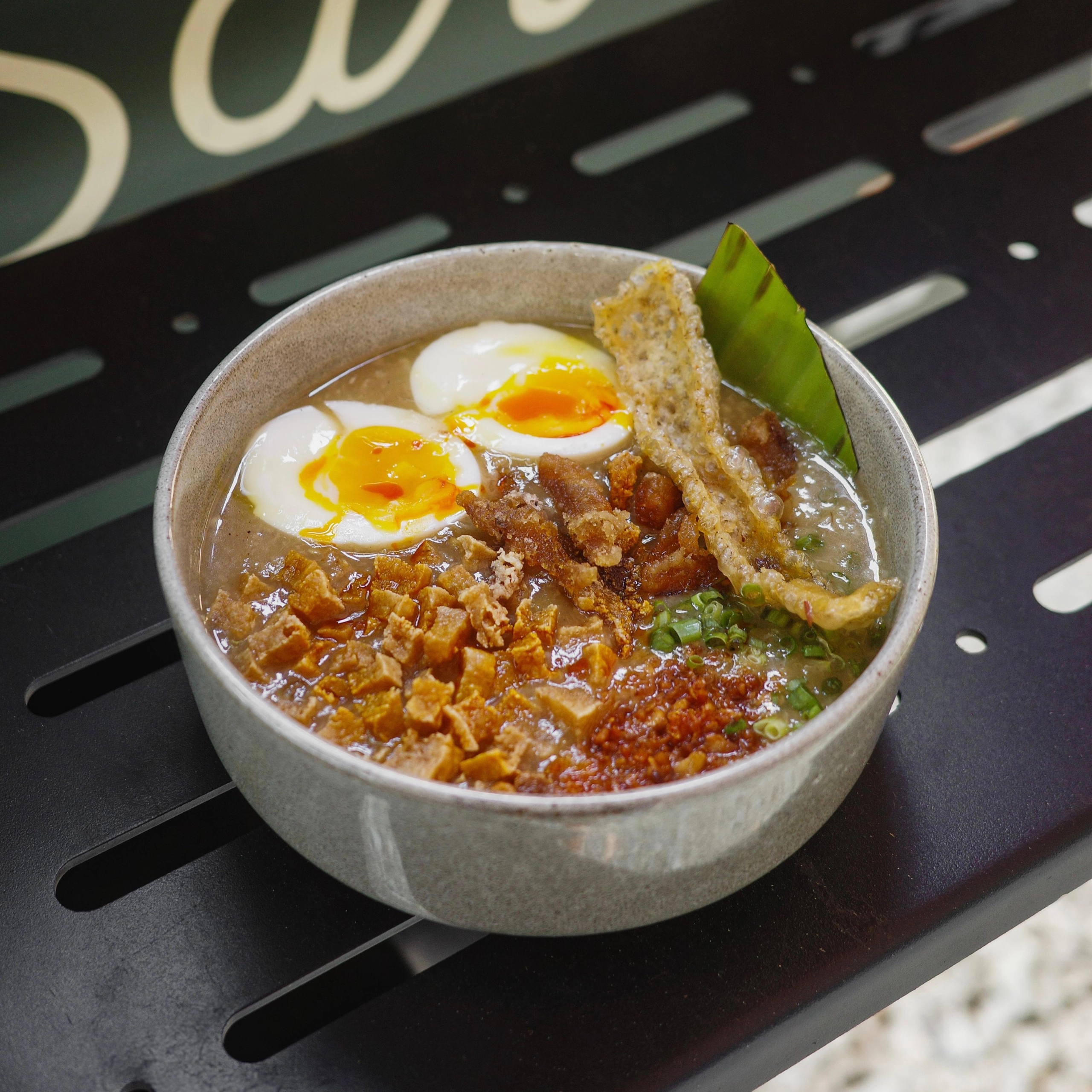 Bowl of soup with soft-boiled eggs, crispy pork bits, and a green leaf garnish.