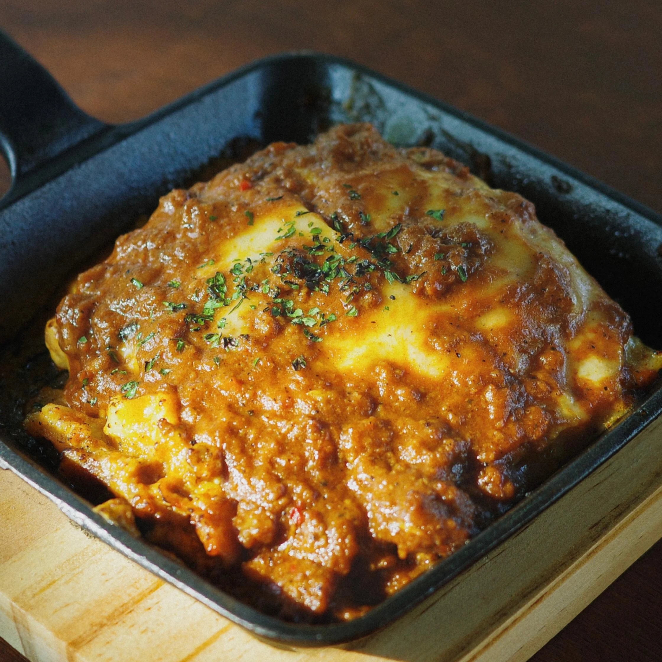 Chicken pieces coated in a glossy tomato sauce with herbs, baking in a dark roasting pan on a wooden surface.