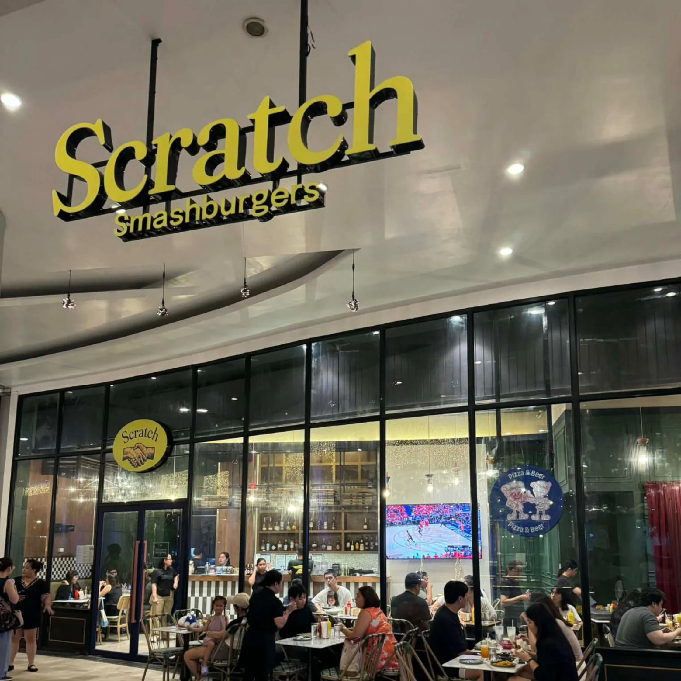Glass storefront of Scratch Smashburgers with a large yellow sign, diners seated inside at tables visible through the glass storefront