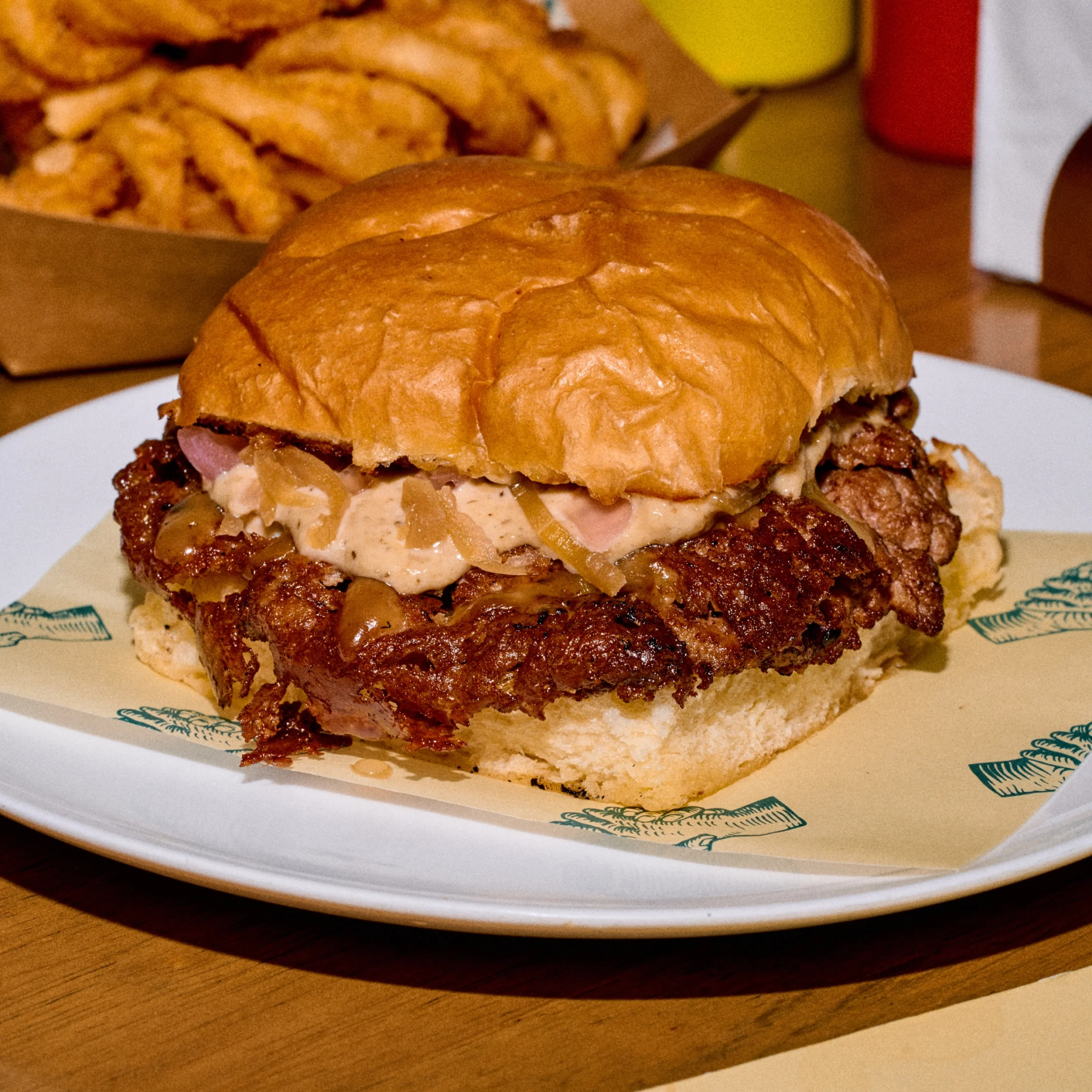 Close-up of a beef hamburger with onions and melted cheese on a toasted bun, on a white plate with a decorative edge.