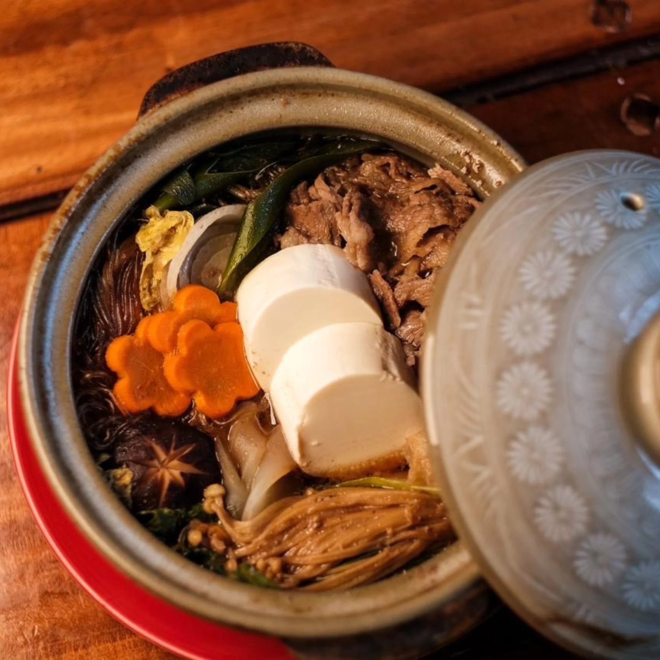 Close-up of a metal pot with shredded beef and vegetables (carrots, corn, greens) visible inside; lid resting nearby.