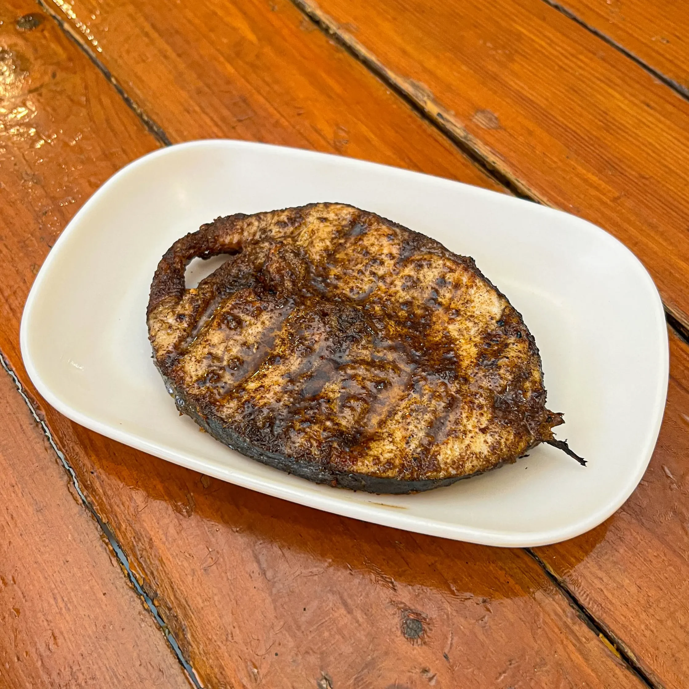 Two heavily charred grilled burgers on a white plate resting on a wooden table.