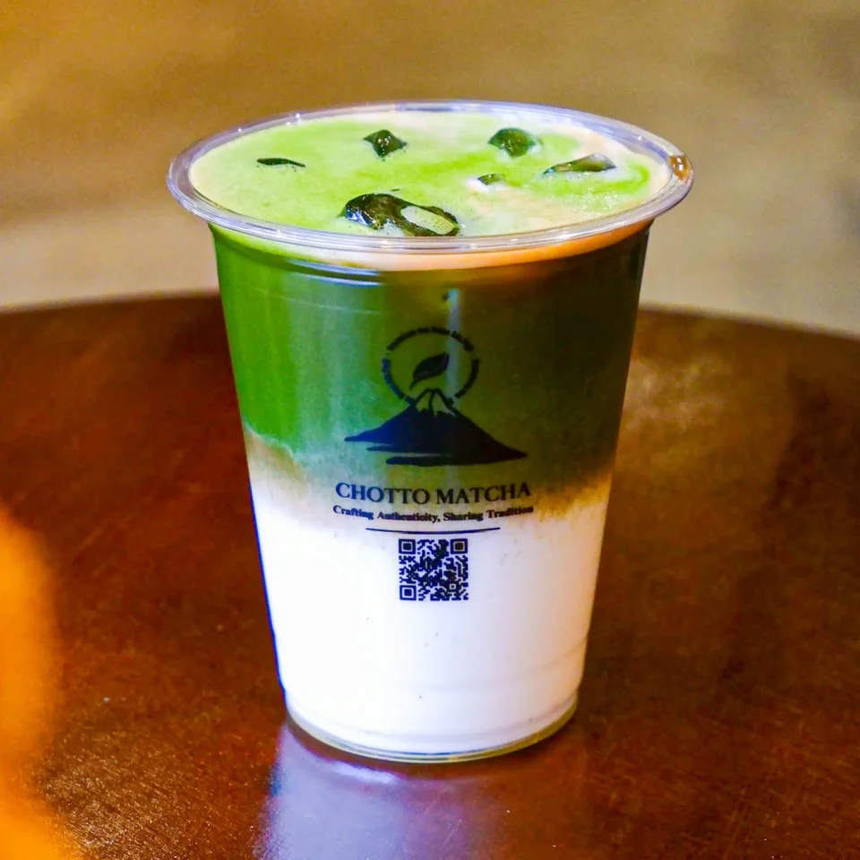 Cold green matcha drink in a white paper cup with a green sleeve and QR code on the label.