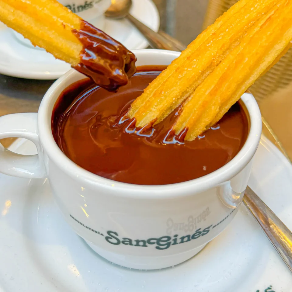Churro dipped into melted chocolate in a white cup.