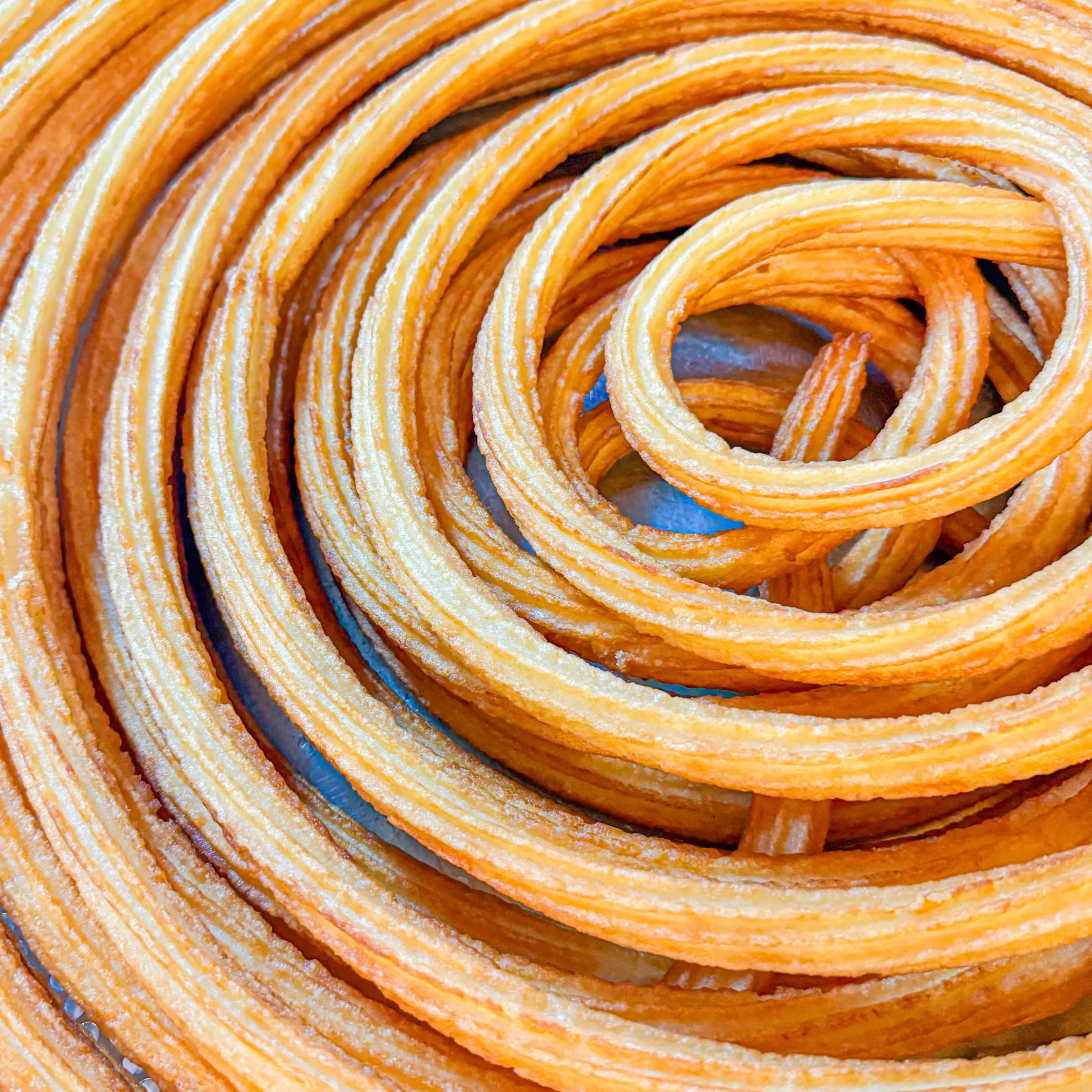 Close-up of orange fried pastry rings curled into spirals, showing ridged surface and glossy glaze.