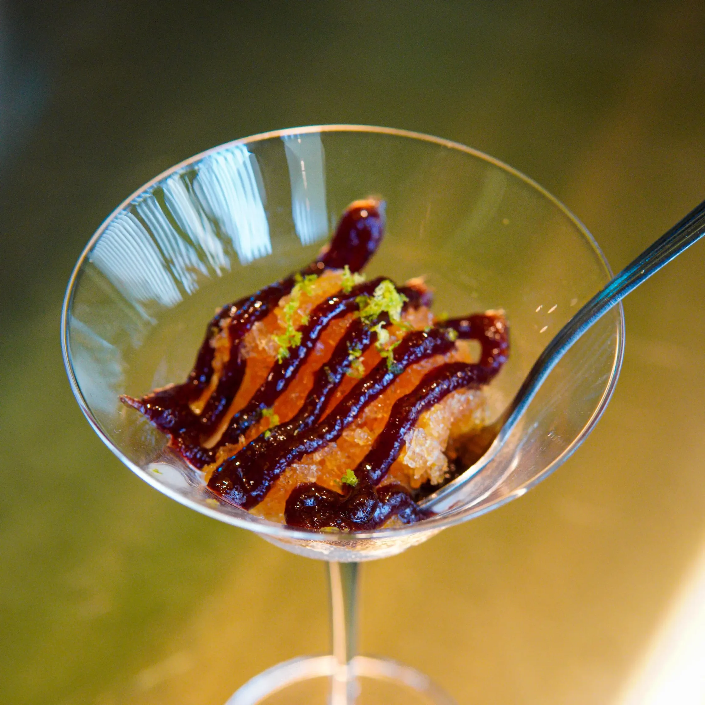 Dessert in a martini glass with chocolate sauce drizzle and a sprinkle of lime zest on top