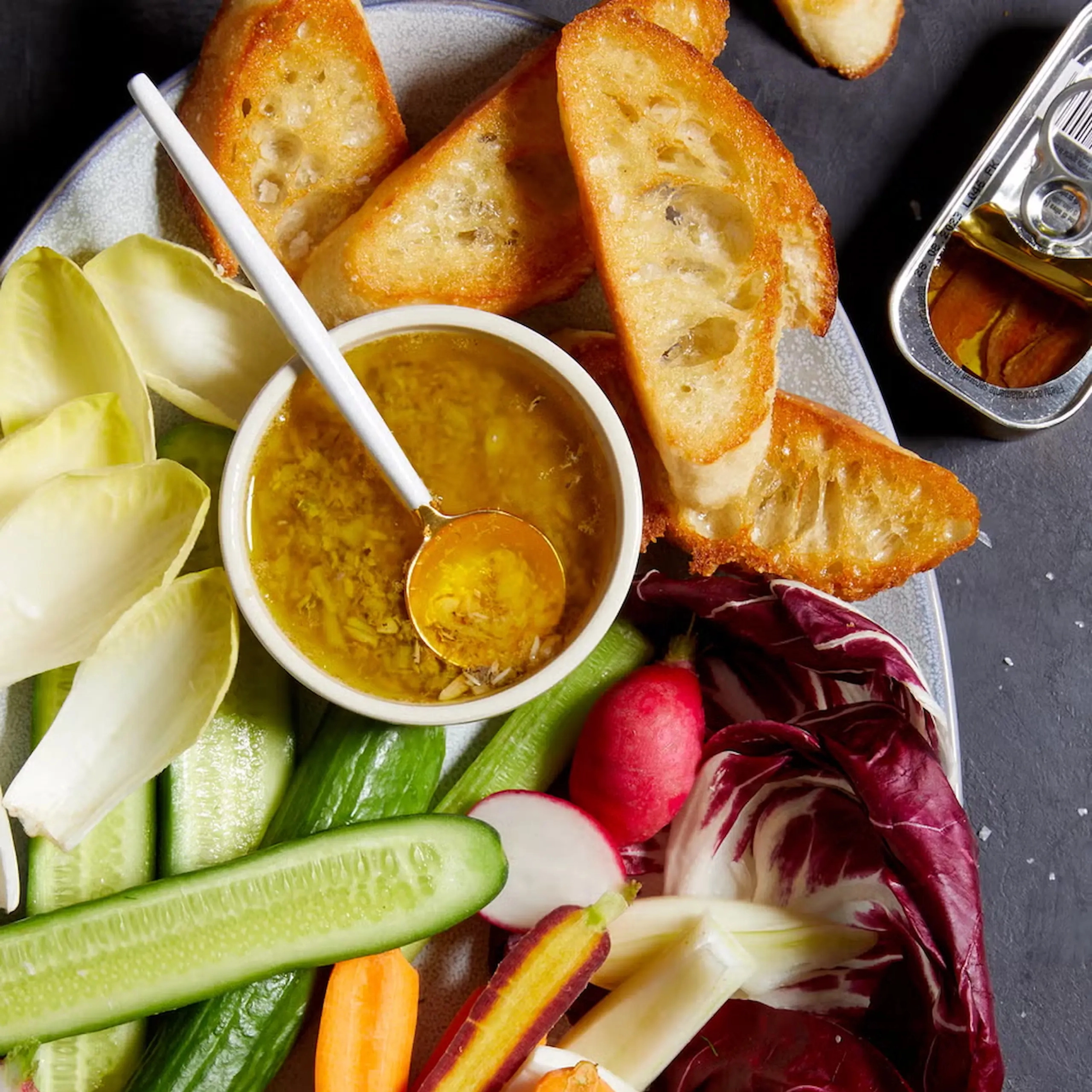Colorful vegetable platter with cucumber and celery sticks, radishes, orange carrot sticks, and leafy greens, served with yellow dips on a plate.