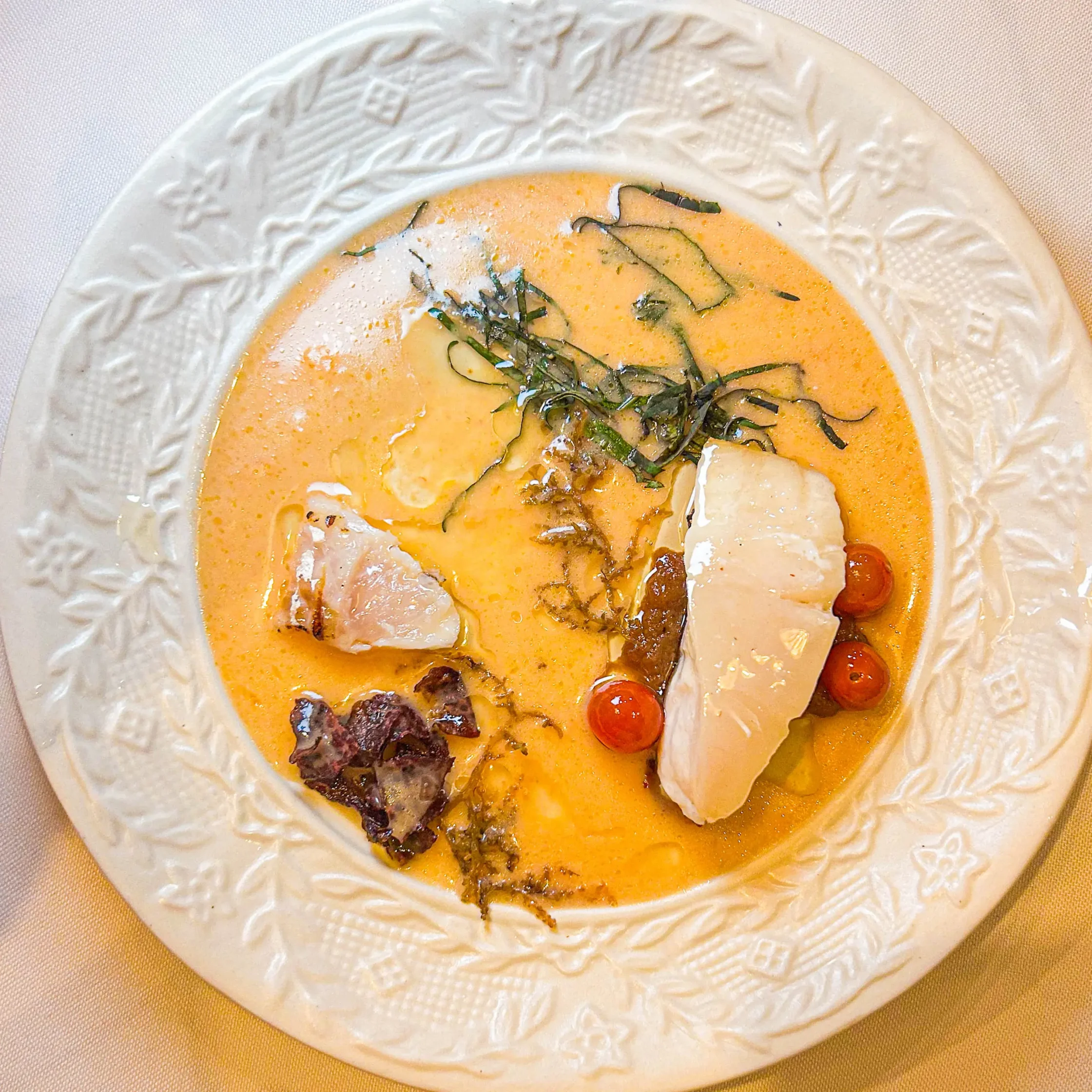 Creamy orange soup in a decorative white plate garnished with herbs and small tomatoes on the side.