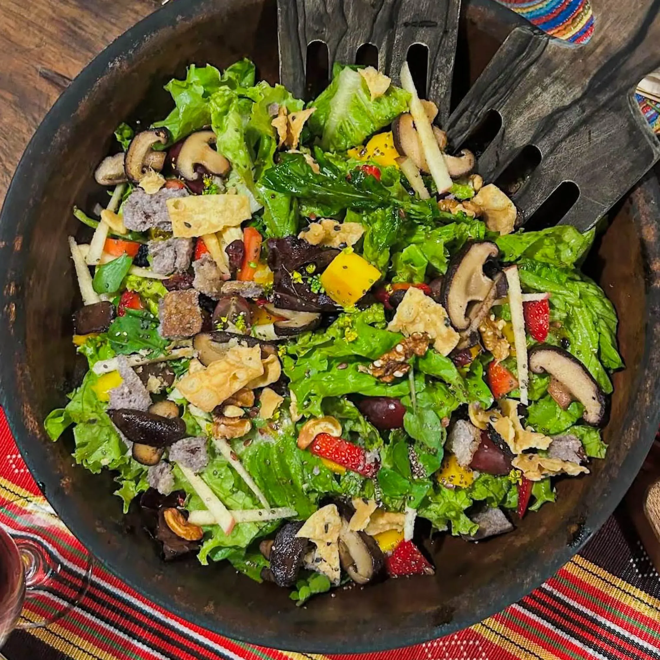 Colorful mixed salad with lettuce, mushrooms, bell peppers and croutons in a dark bowl on a red plaid tablecloth.