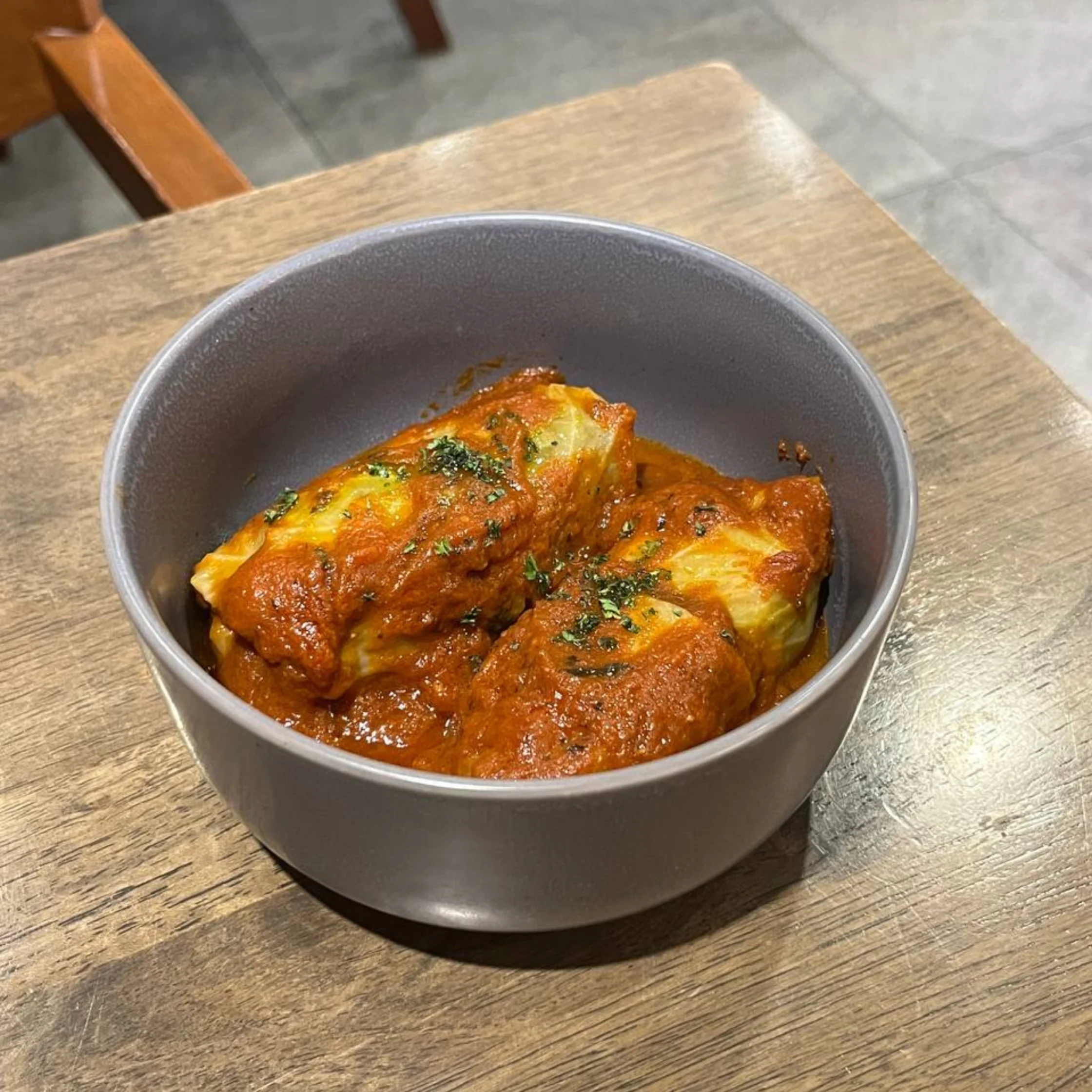 Bowl of lasagna with tomato sauce and parsley on a wooden table.