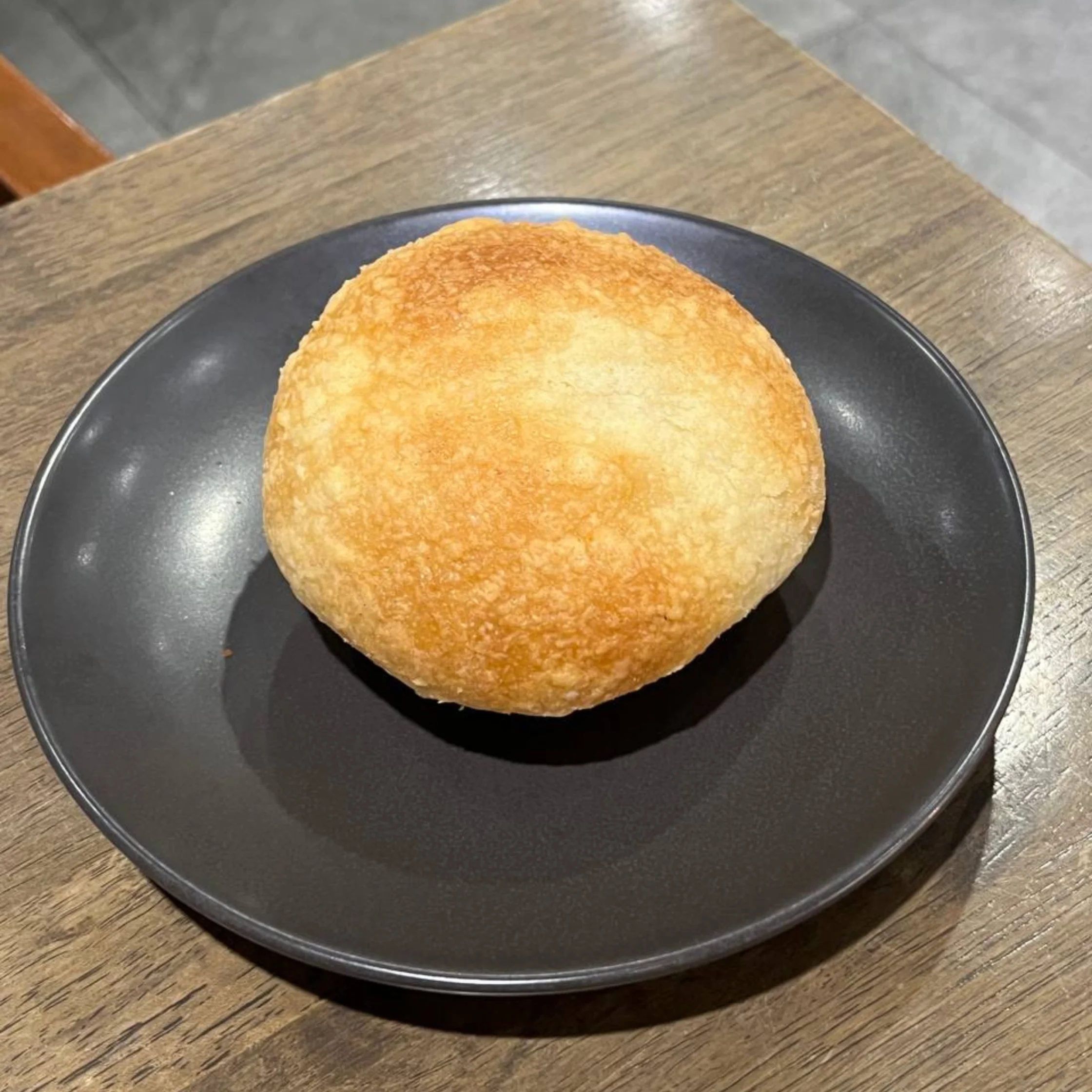 Golden brown fried pastry on a dark plate resting on a wood table, close-up appearance.