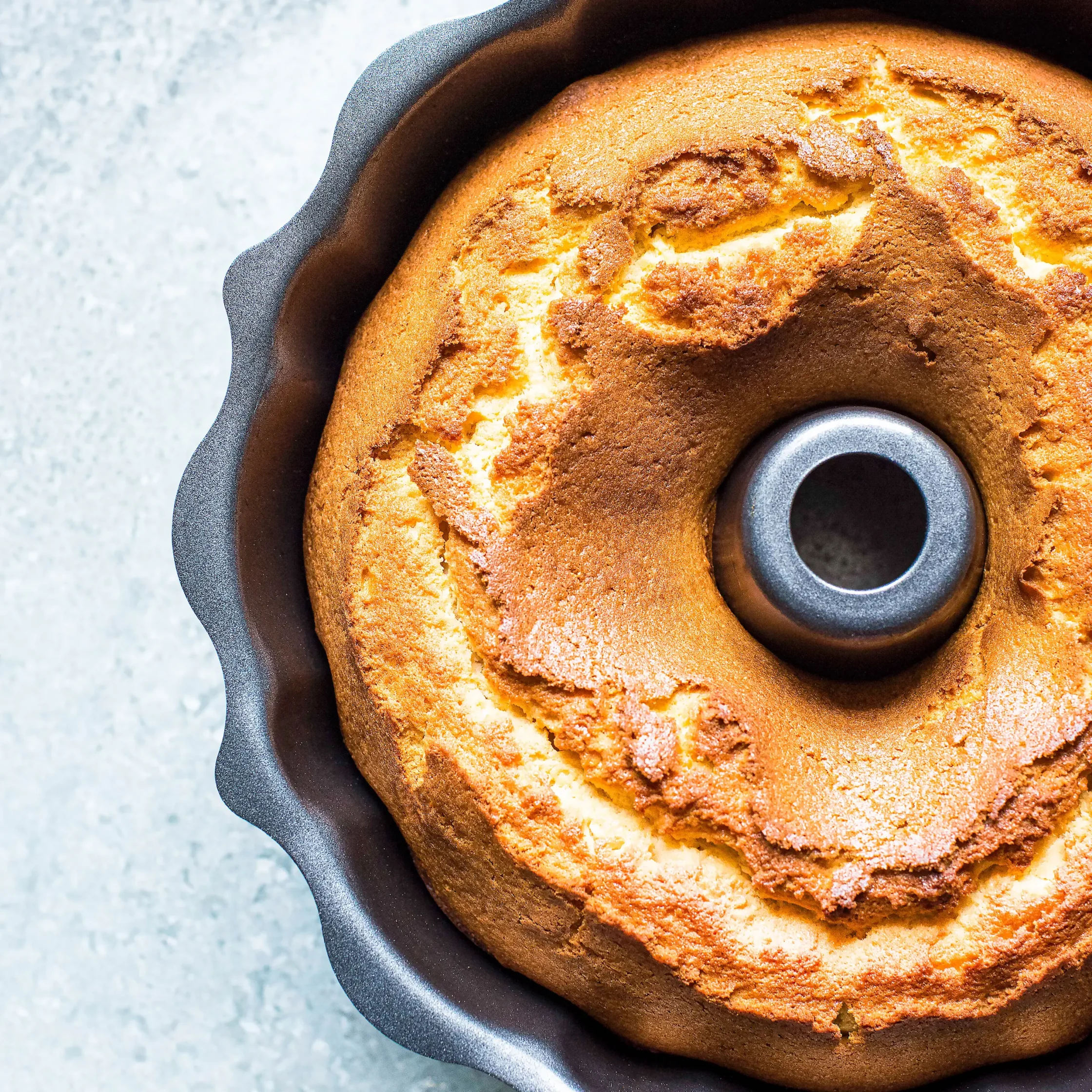 Close-up of a golden-brown Bundt cake with a textured, cracked crust in a dark baking pan.