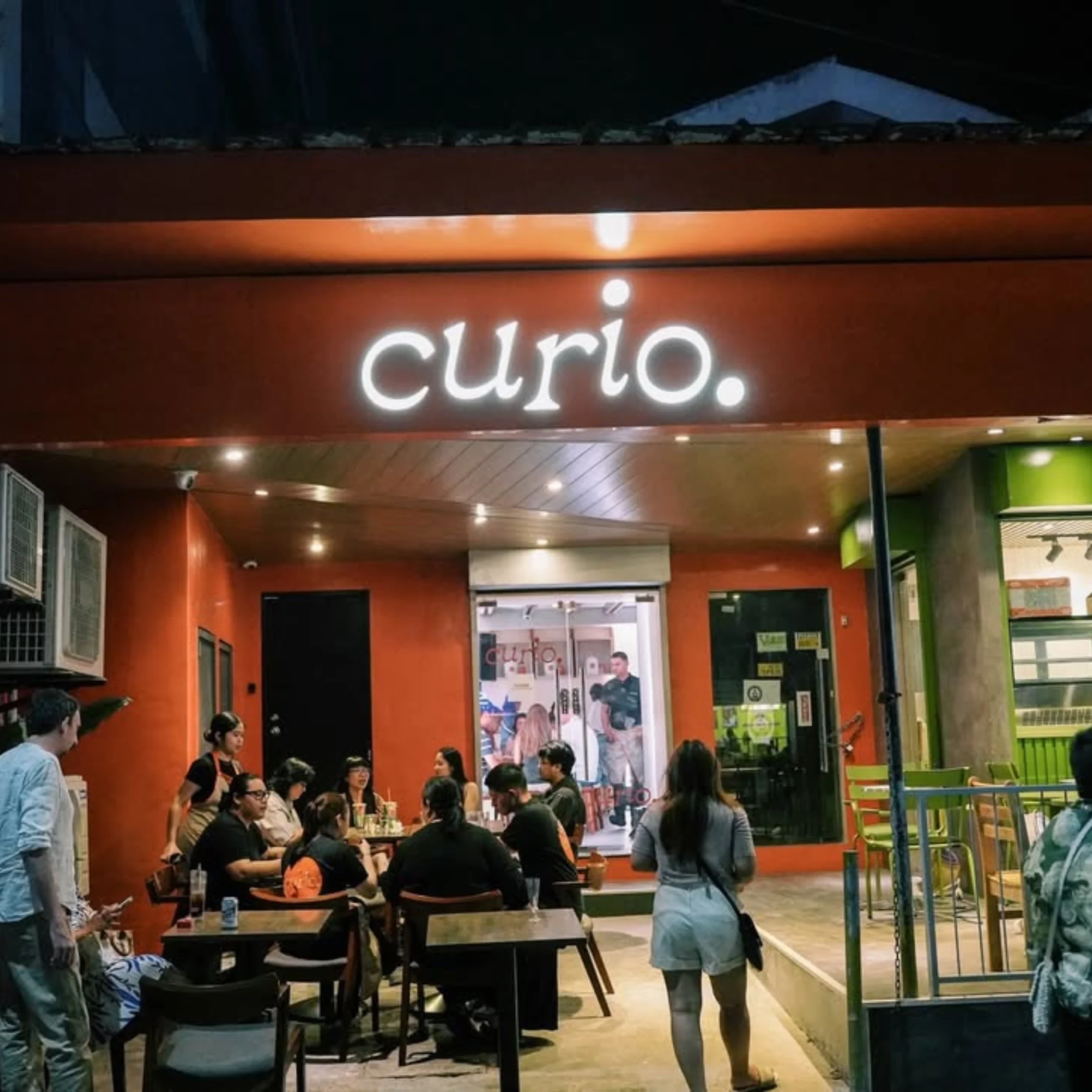 Casual cafe scene inside a shopping center with orange walls, several people seated at tables and talking.