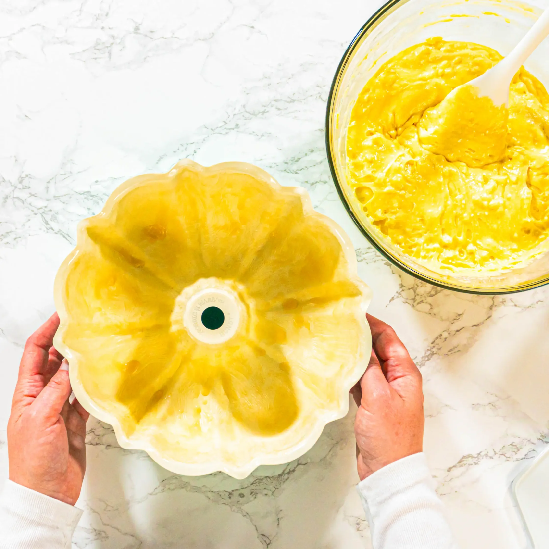 Hands holding a round pie crust filled with yellow custard on a white marble surface