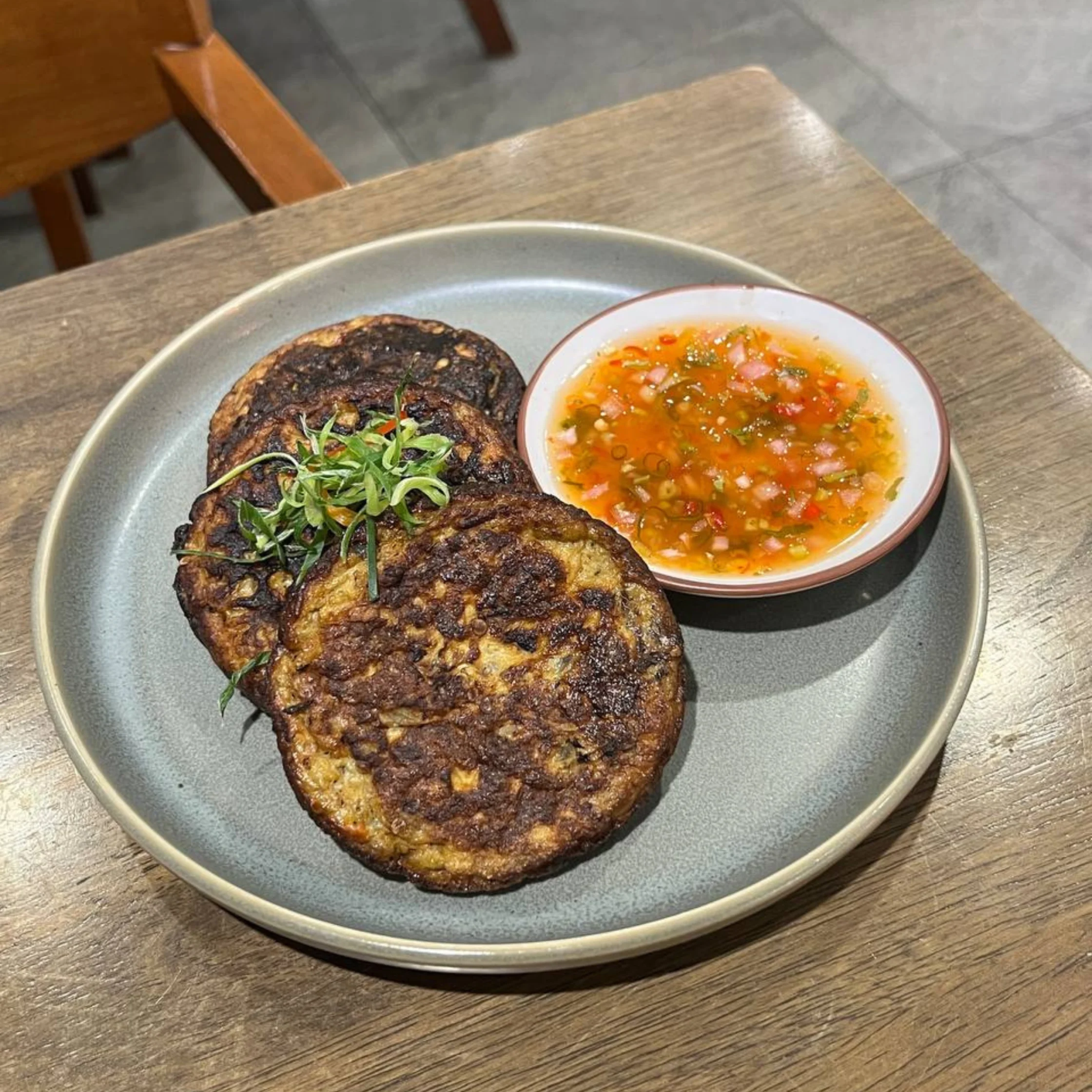 Two grilled patties on a gray plate with a small bowl of chunky salsa on the side, set on a wooden table.