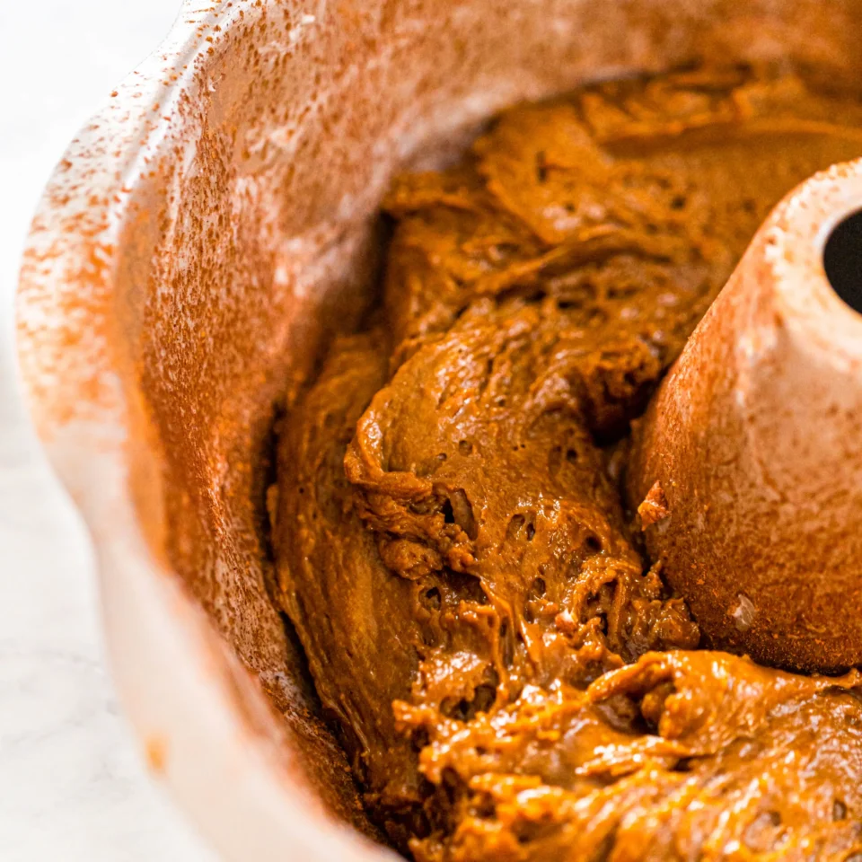 Close-up of a freshly baked loaf with a dark, glossy crust and dense, brown crumb showing through.