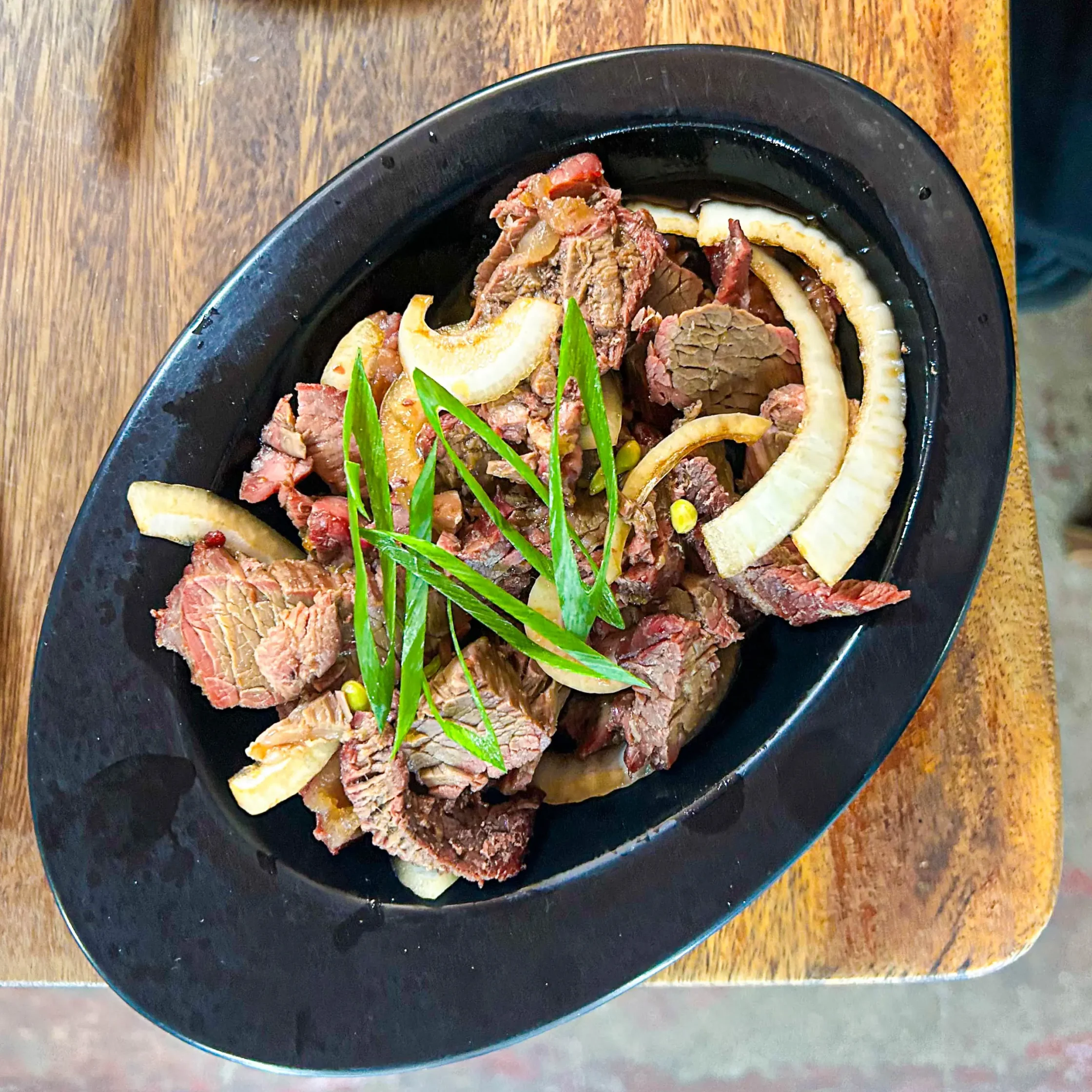 Thinly sliced roast beef arranged on a dark plate with lemon wedges and green garnish.
