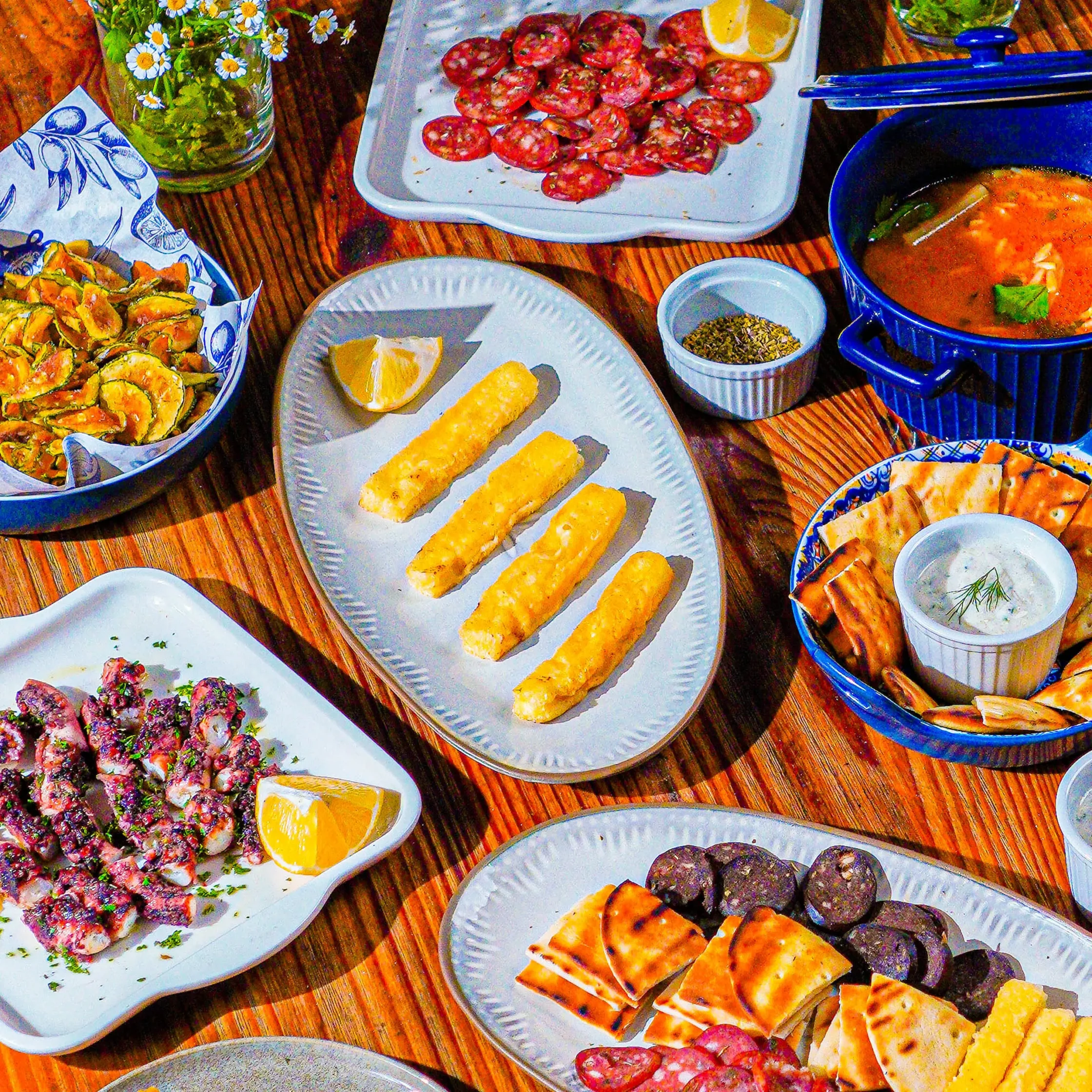 Assorted tapas on plates: fried pastries, lemon wedges, and sliced sausage on a wooden table.