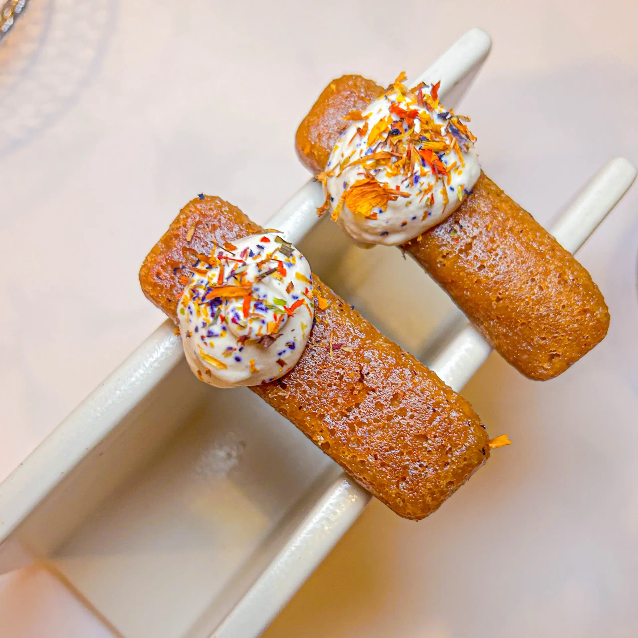 Skewered fried dough bites topped with white cream and colorful sprinkles.