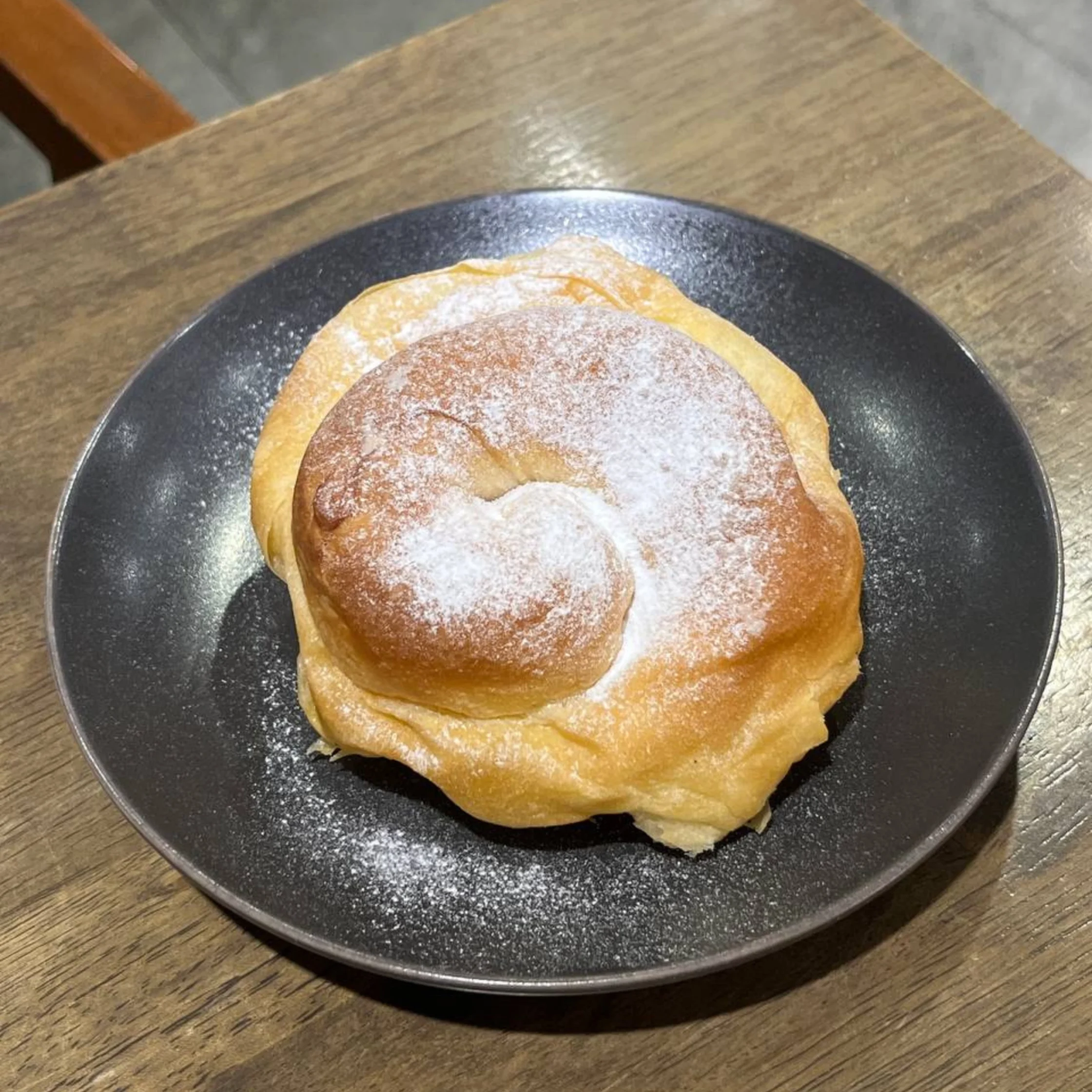 Coiled pastries dusted with powdered sugar on a dark plate atop a wooden table