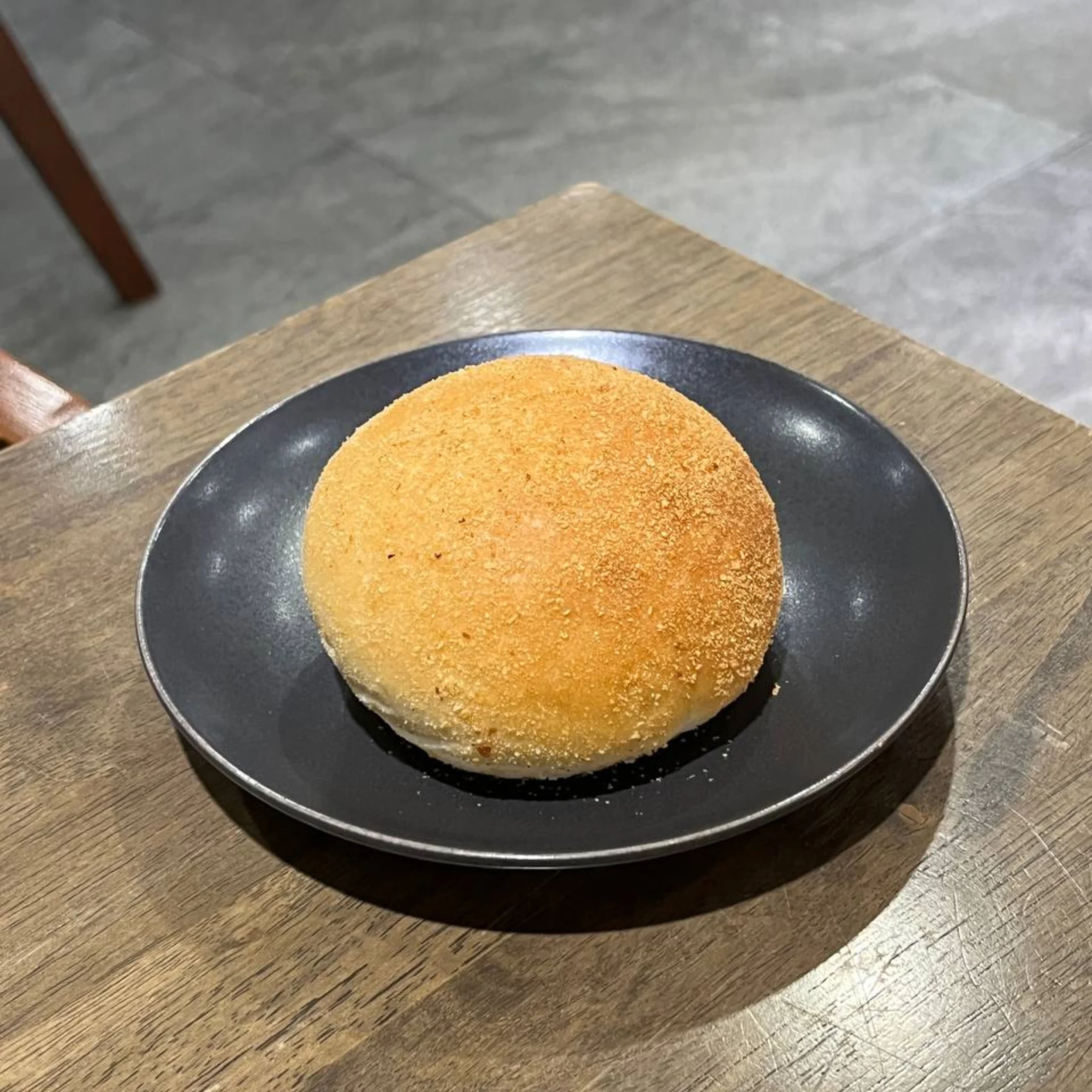 Round, breaded fried patty on a dark plate set on a wooden table