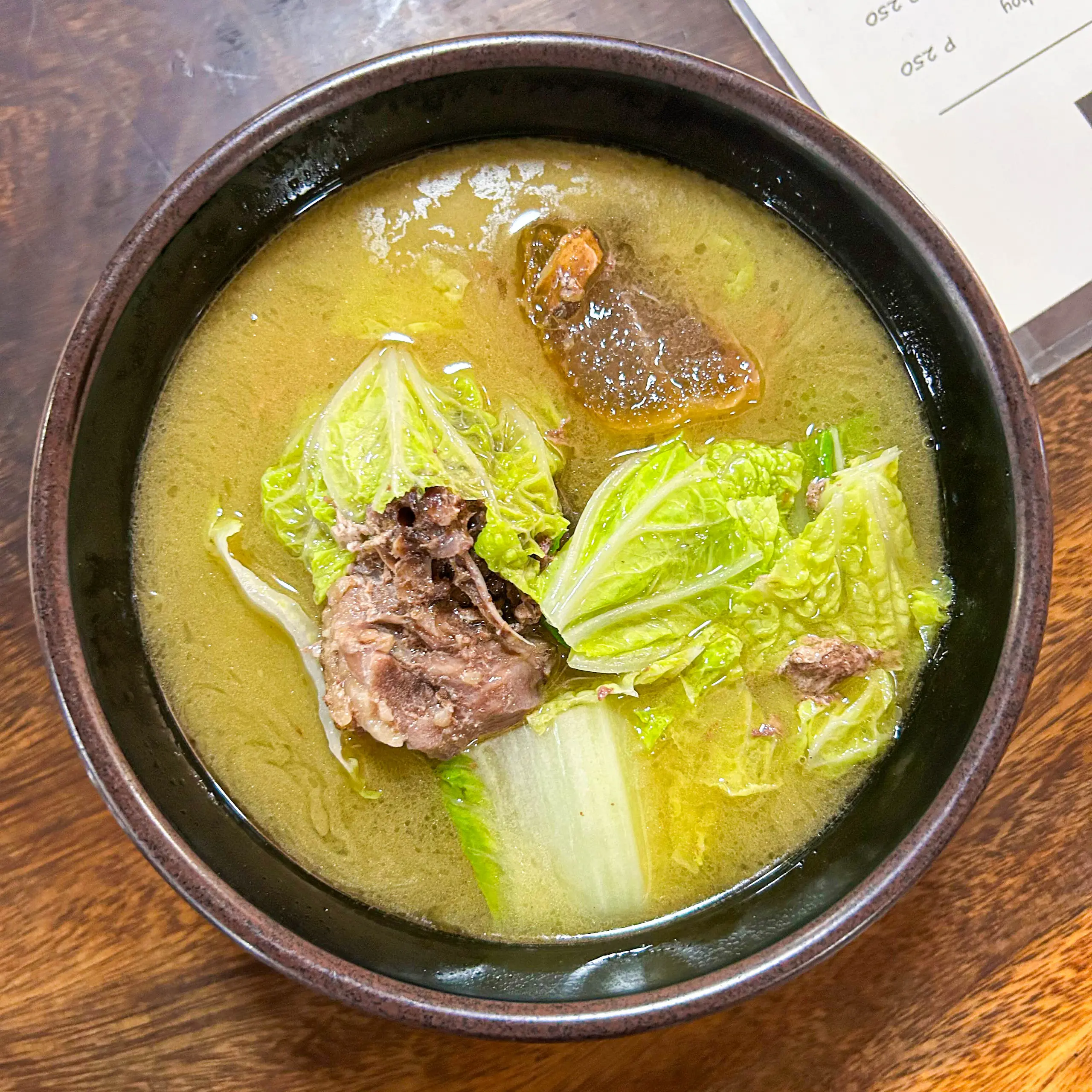 Bowl of beef and cabbage soup in a dark ceramic pot on a wooden table. (top-down view)