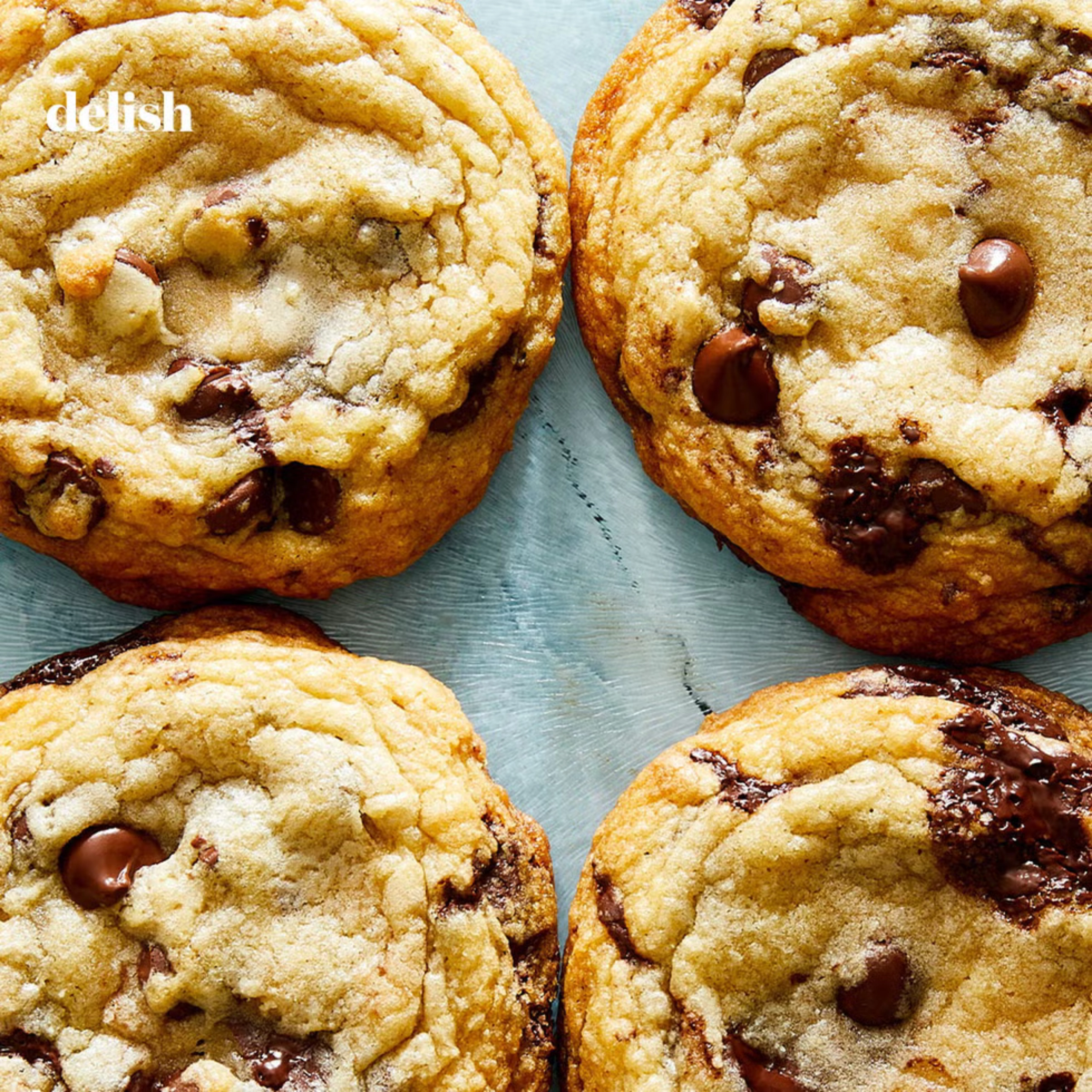 Close-up of warm chocolate chip cookies on a blue surface, showing crumbly texture and melted chocolate.