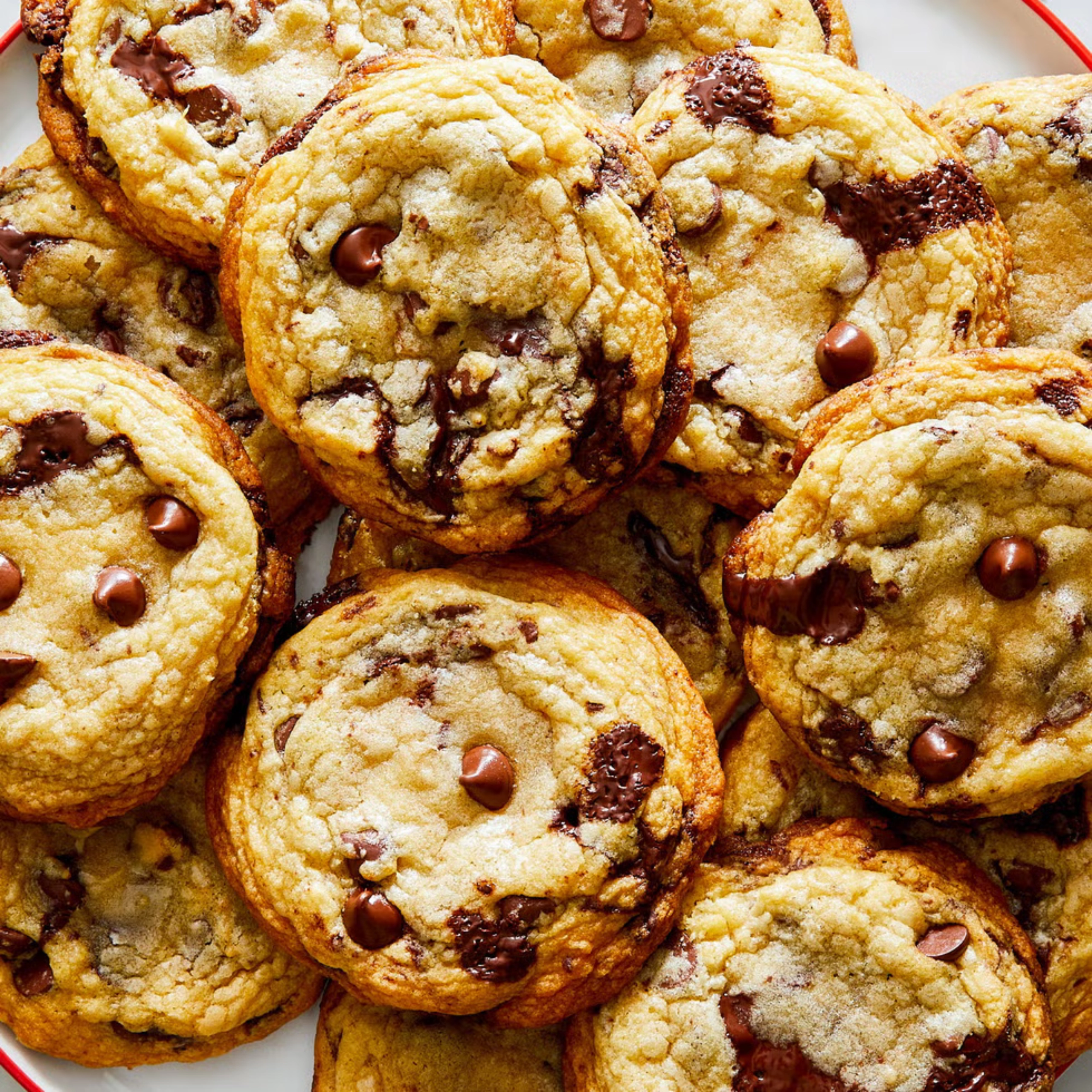 Close-up of a pile of chocolate chip cookies on a plate, showing melted chocolate chips and golden edges.