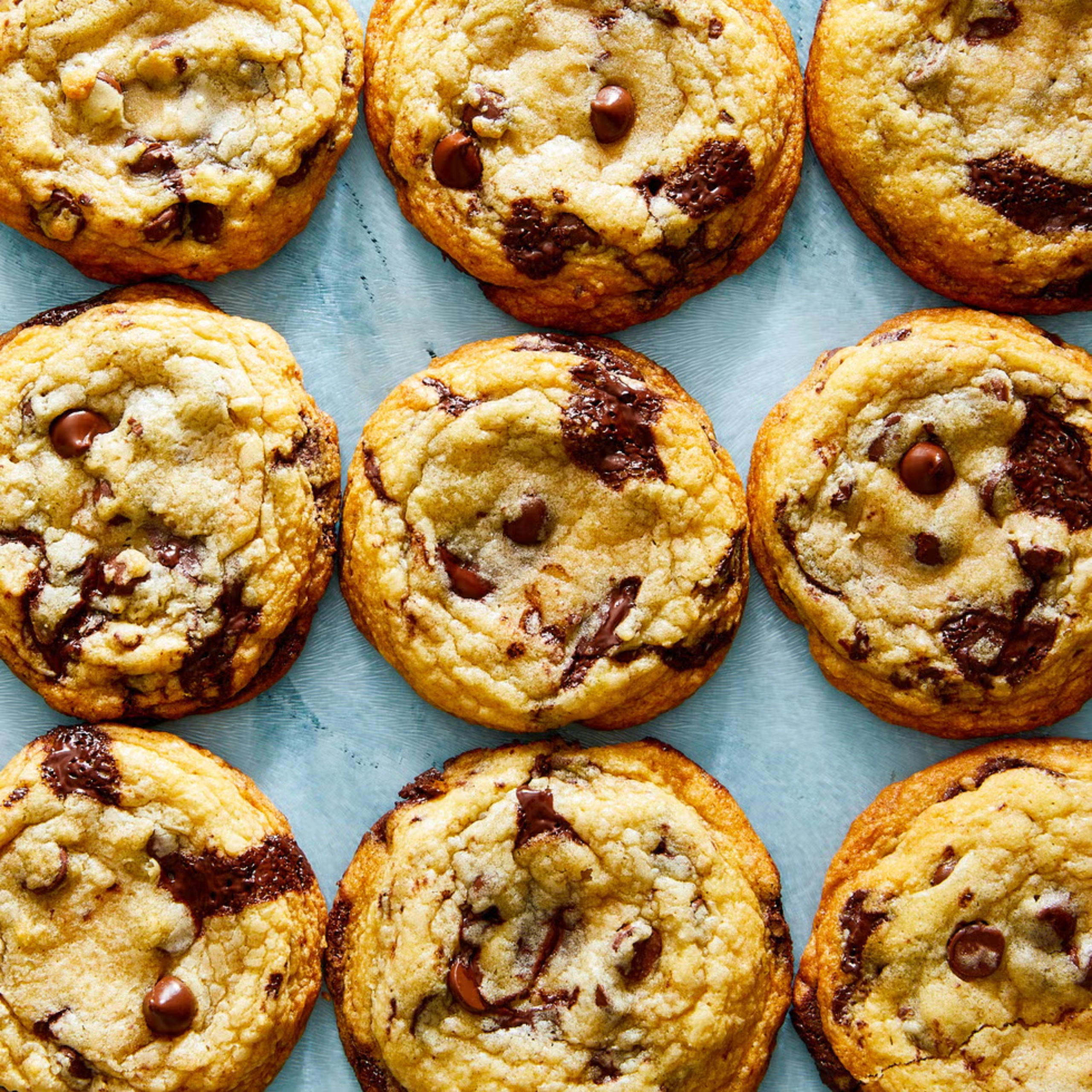 Several chocolate chip cookies arranged on a blue surface; golden, crumbly cookies with melted chocolate chips visible.