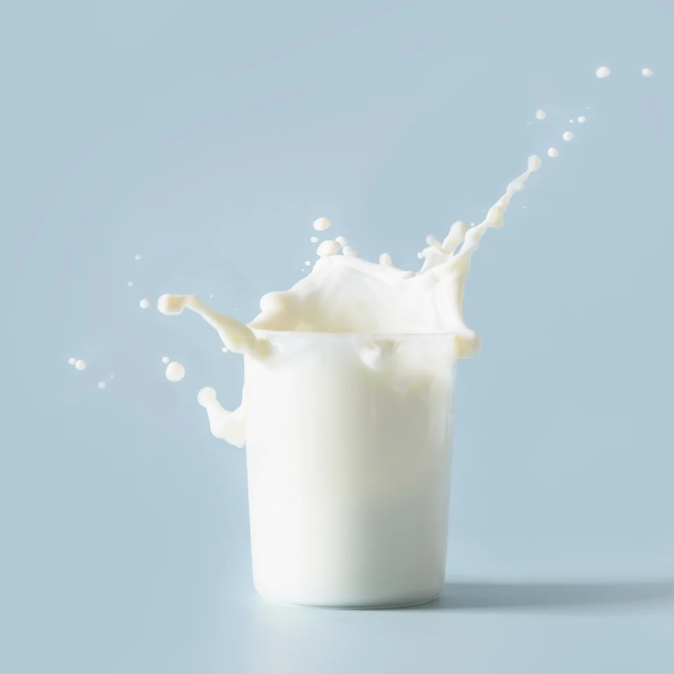 Pouring milk splash emerging from a glass against a pale blue background.
