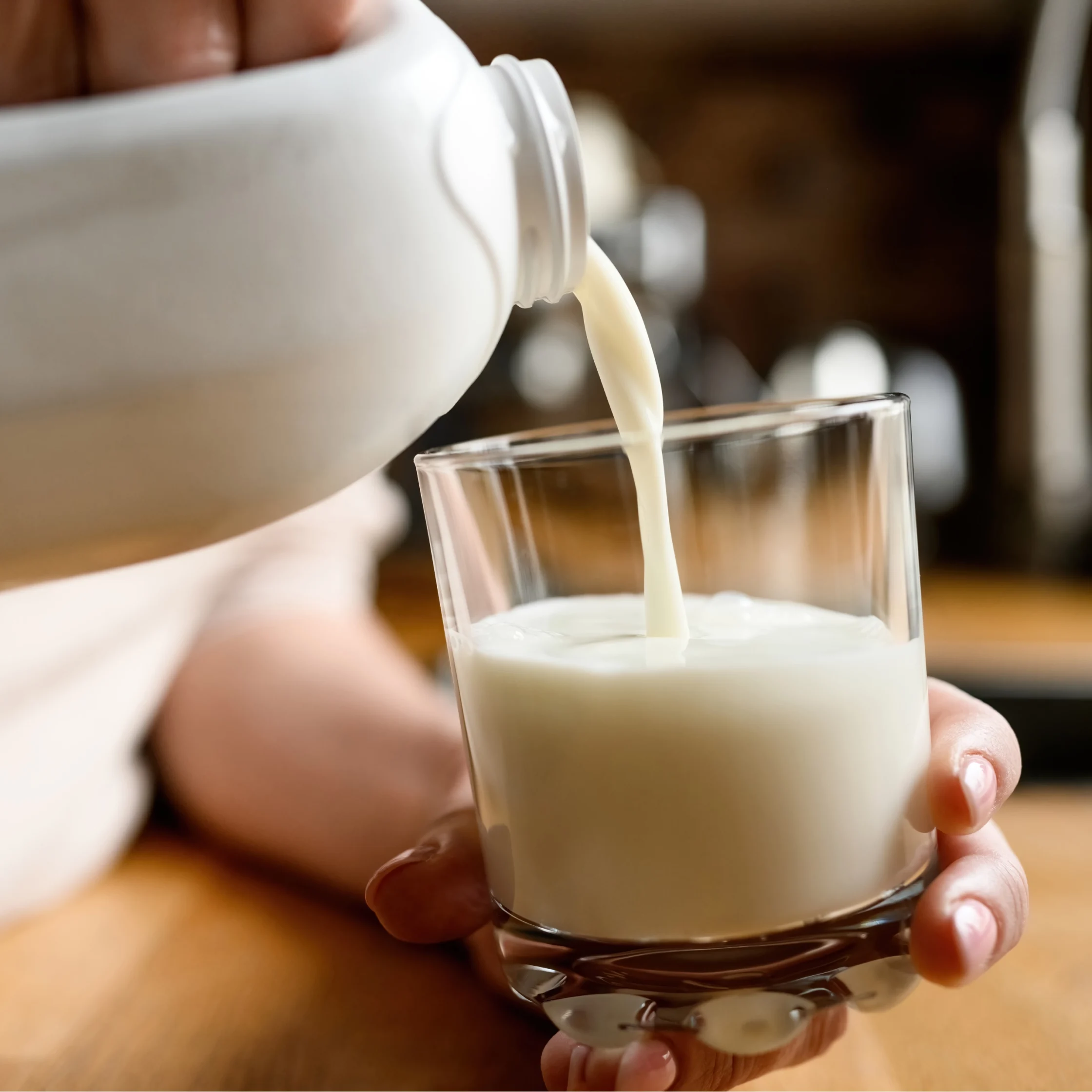 Milk is poured from a bottle into a glass, with a small hand stabilizing the container nearby.