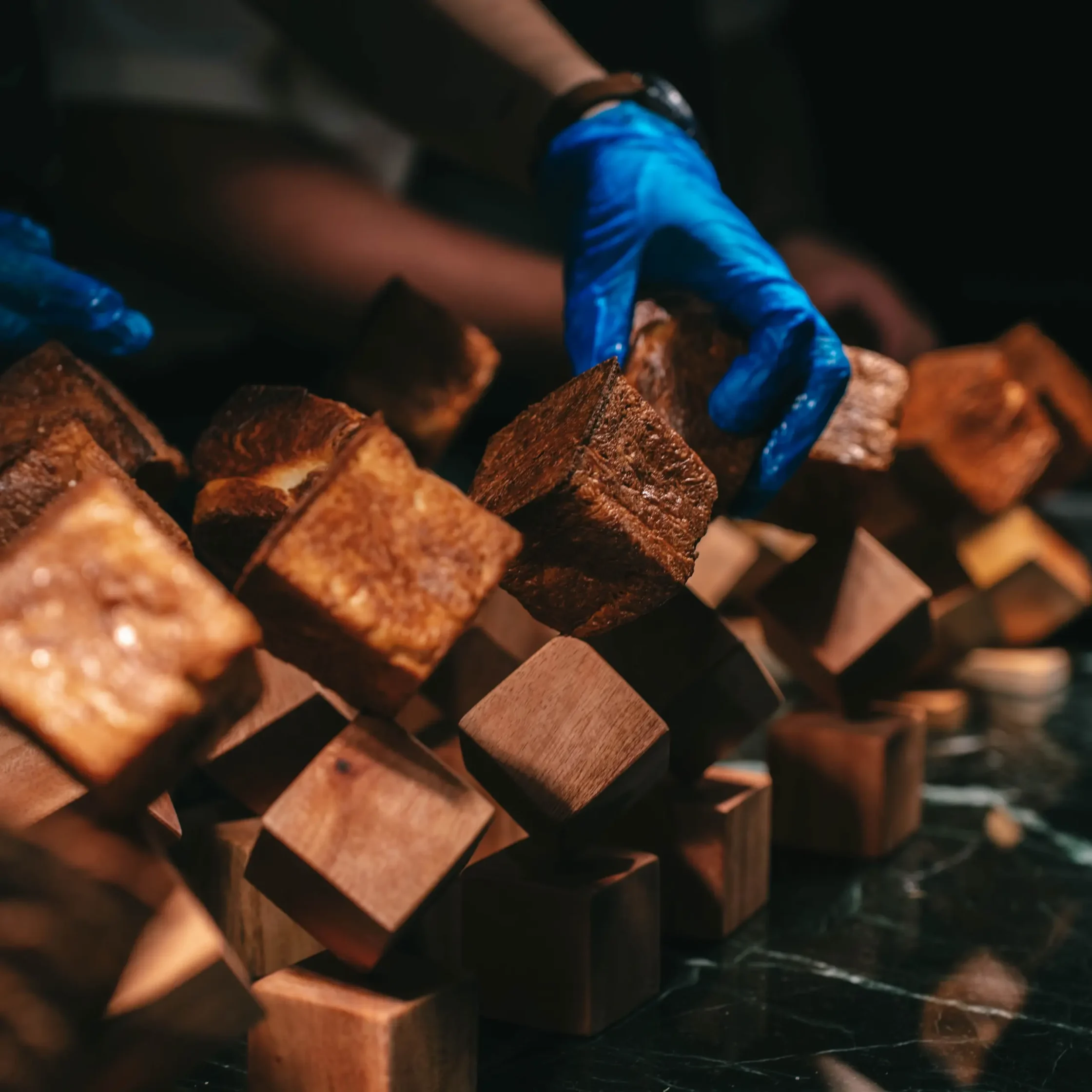 Close-up of brown sugar cubes with a blue-gloved hand reaching in.
