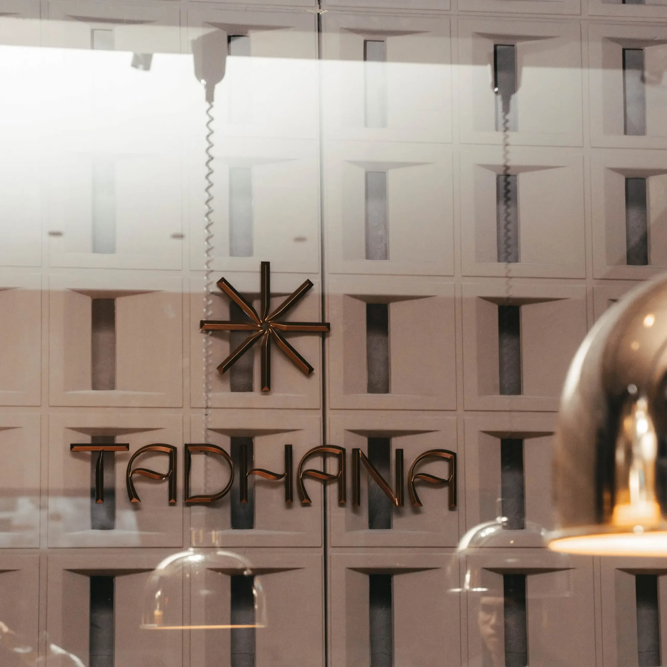 Shop window display: bronze starburst sculpture on a gray paneled wall, with partial storefront letters visible