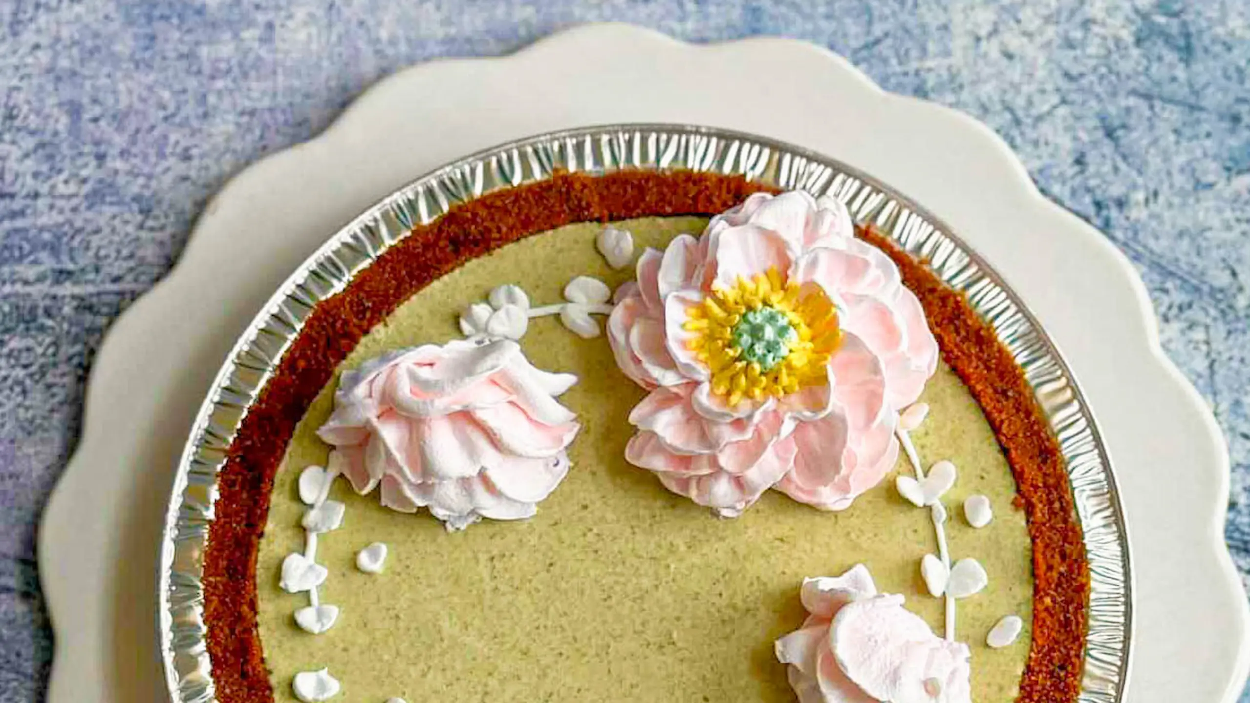 Cake decorated with large pink and white frosting flowers and scattered white petal accents.