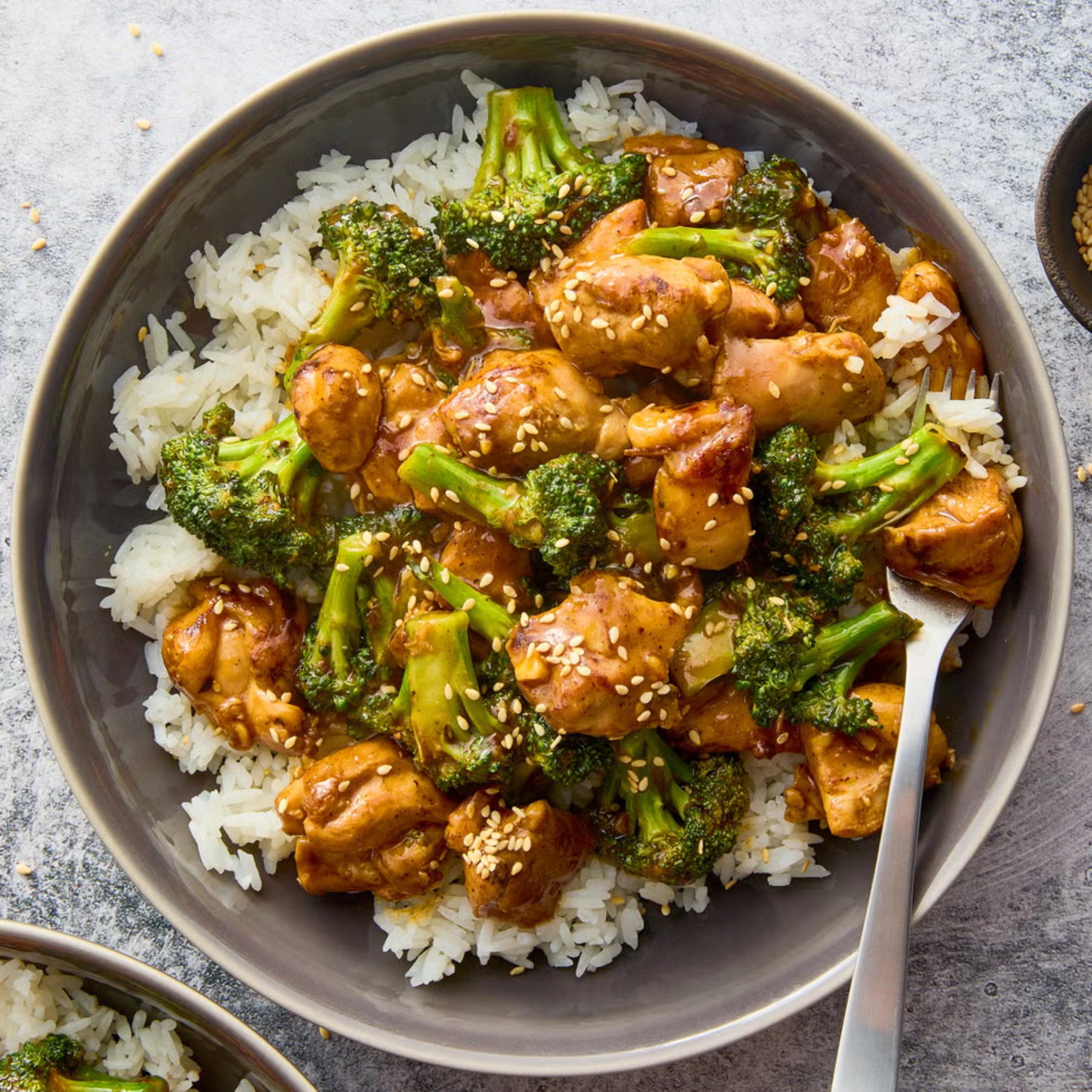 Chicken and broccoli stir-fry over white rice with sesame seeds in a bowl of sauce