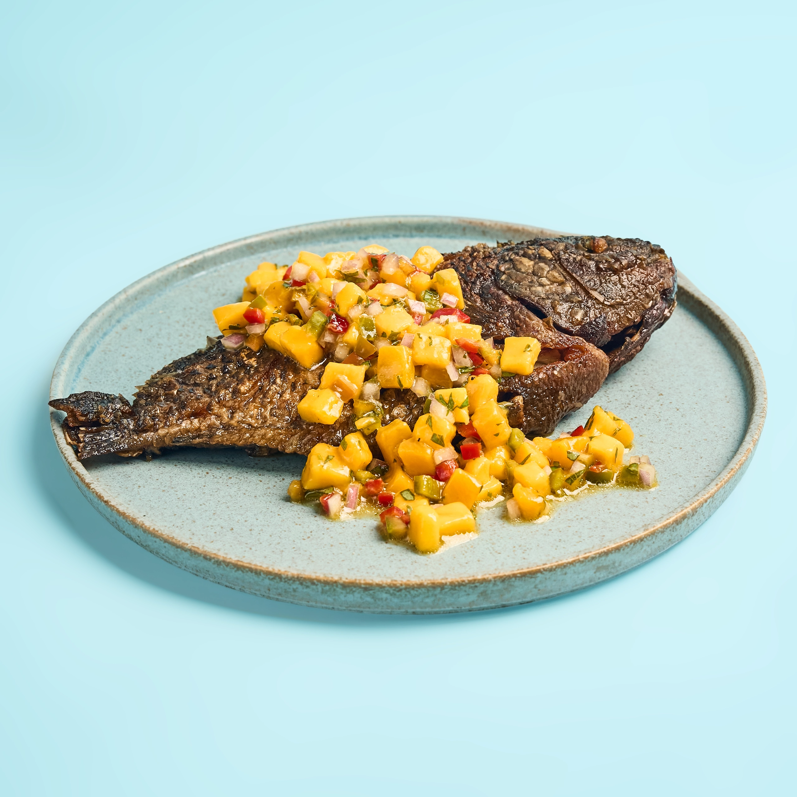 Beef steak topped with a chunky mango salsa on a light blue plate with a blue background.