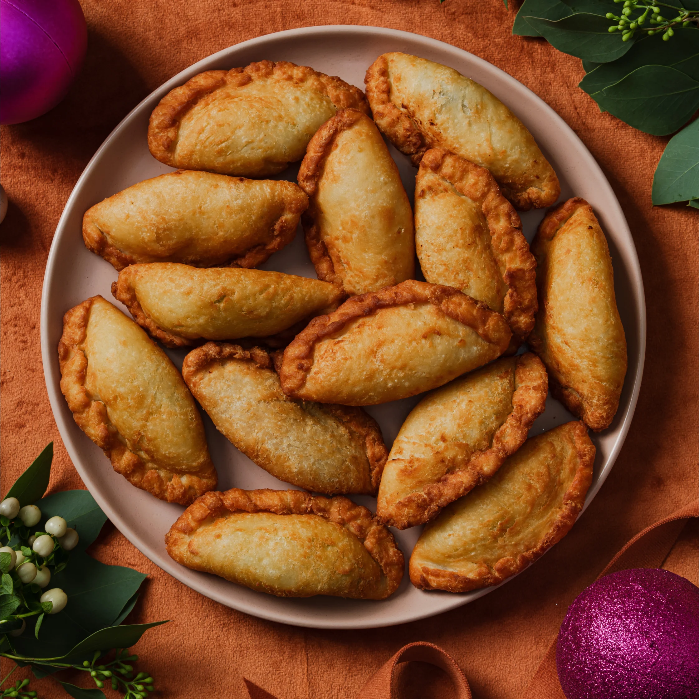 Plate of golden fried Filipino empanadas arranged on a round serving dish with festive decorations around it.